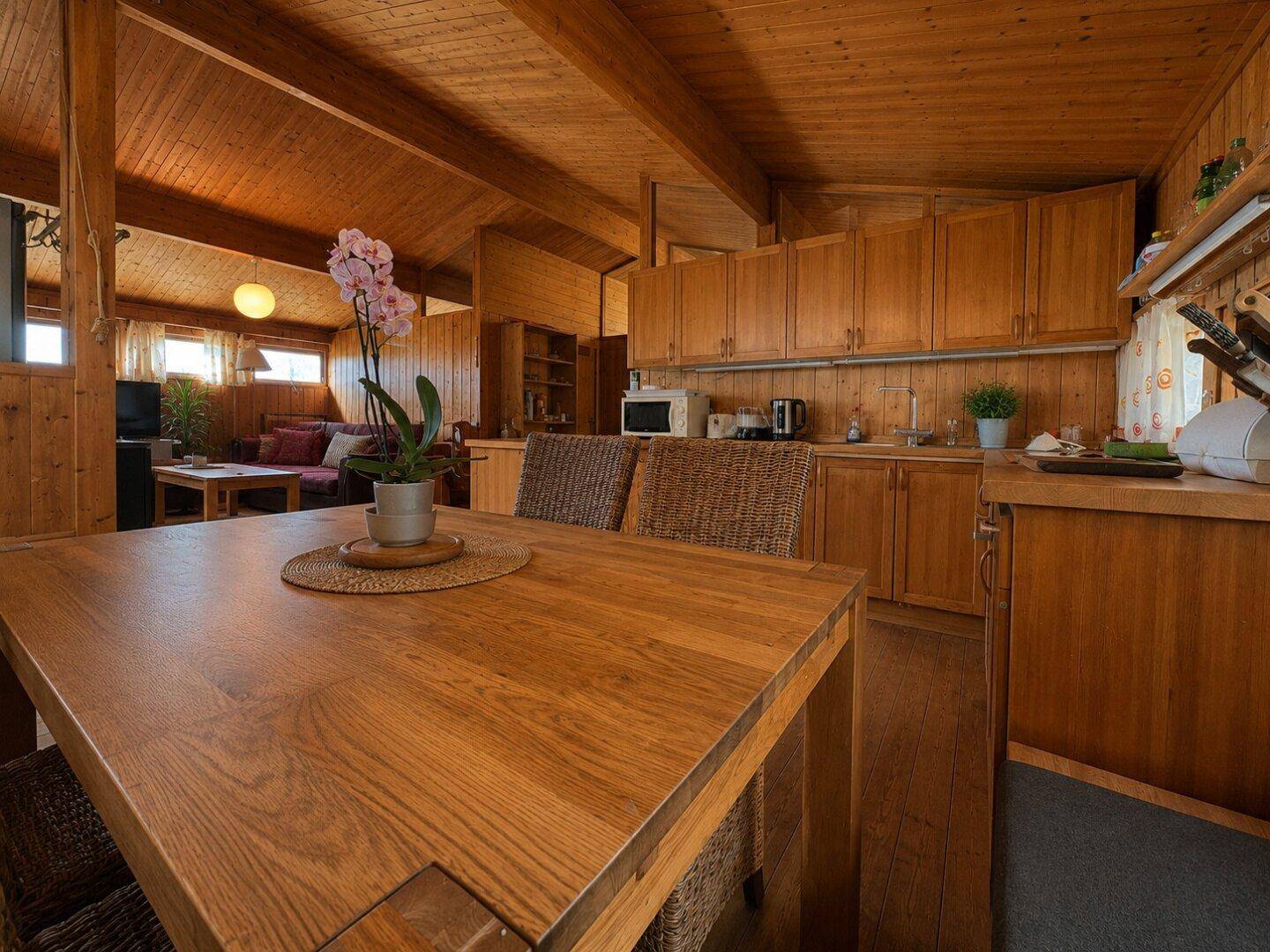 Essbereich mit Holztisch und Blick auf die offene Holzküche mit Einbaugeräten.