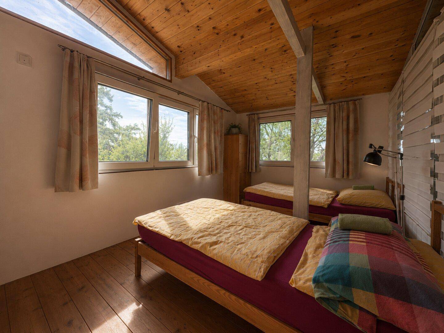 Helles Schlafzimmer mit mehreren Betten, Holzboden und schrägen Decken.