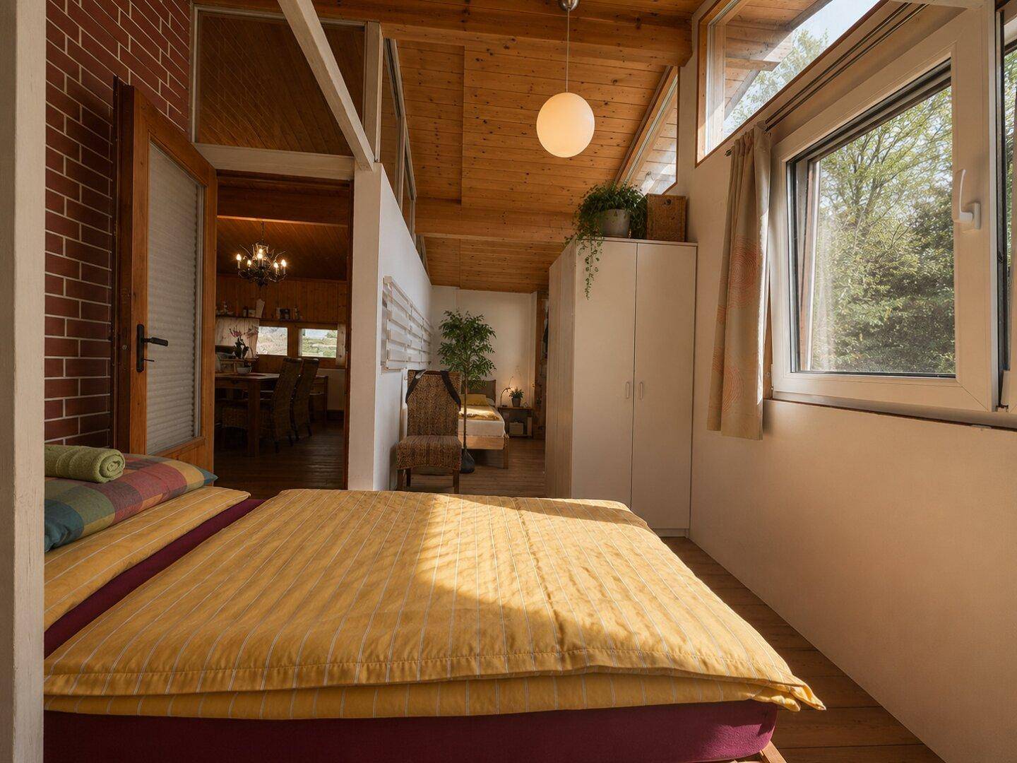 Schlafzimmer mit Holzboden, hellen Wänden und Blick in den offenen Wohnbereich.