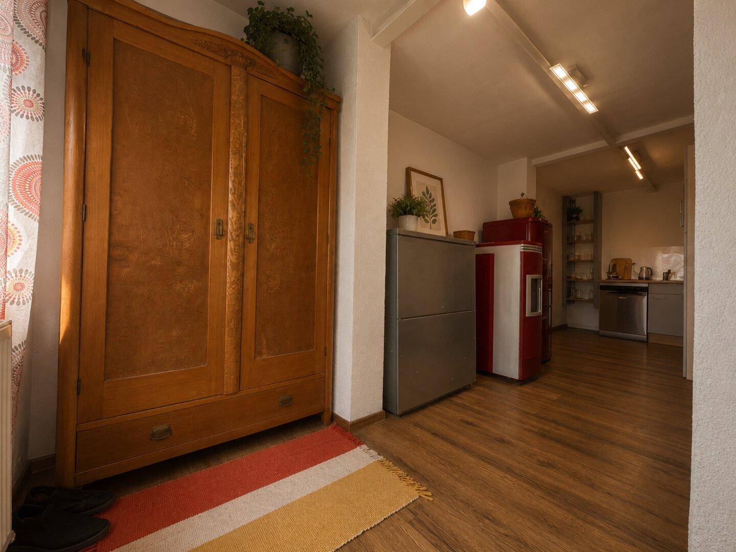 Eingangsbereich mit Holzschrank und Blick in die moderne Küche des Erdgeschosses.