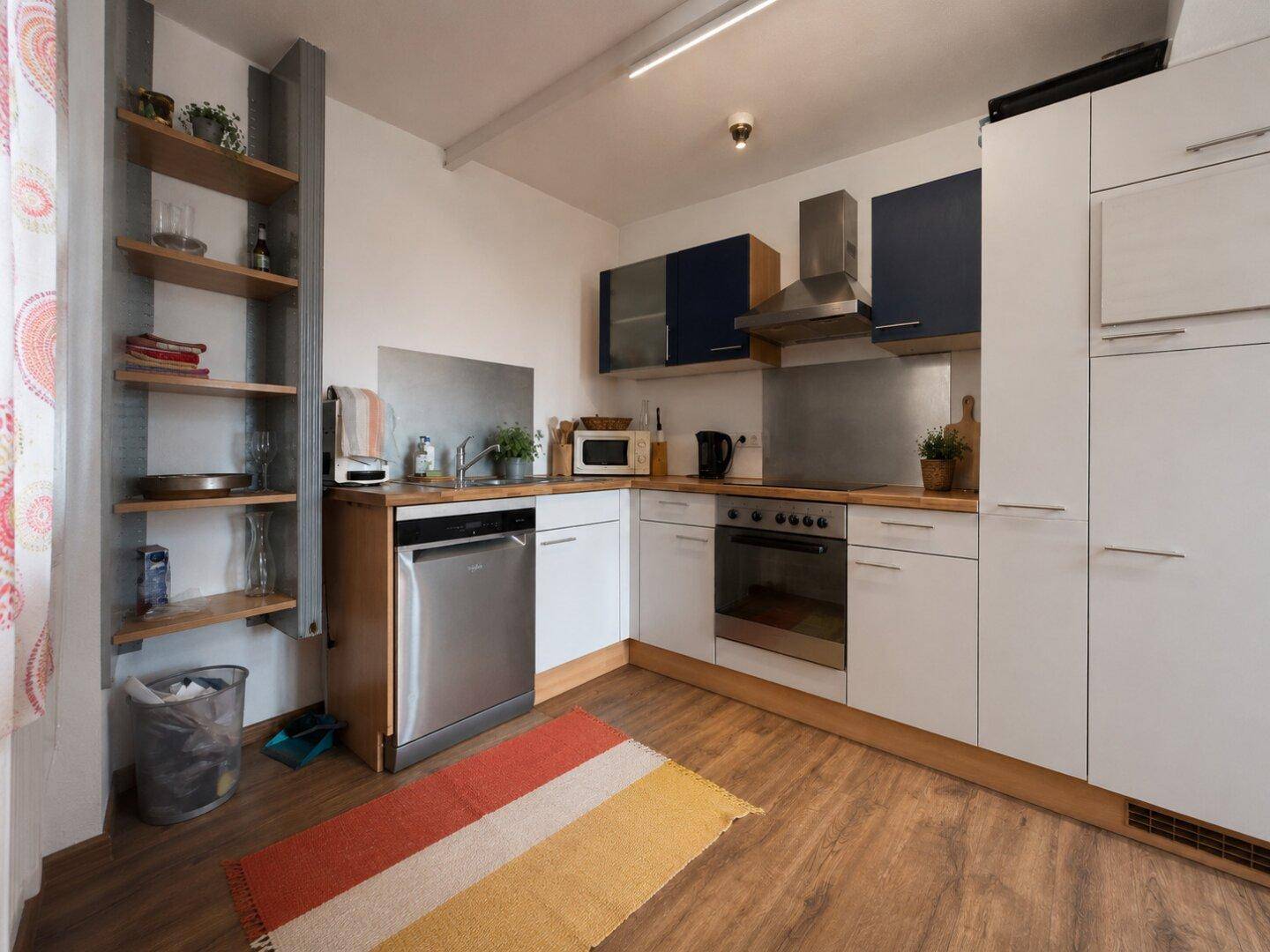 Moderne Küche mit weißen und blauen Schränken, Einbaugeräten und Holzarbeitsplatte.