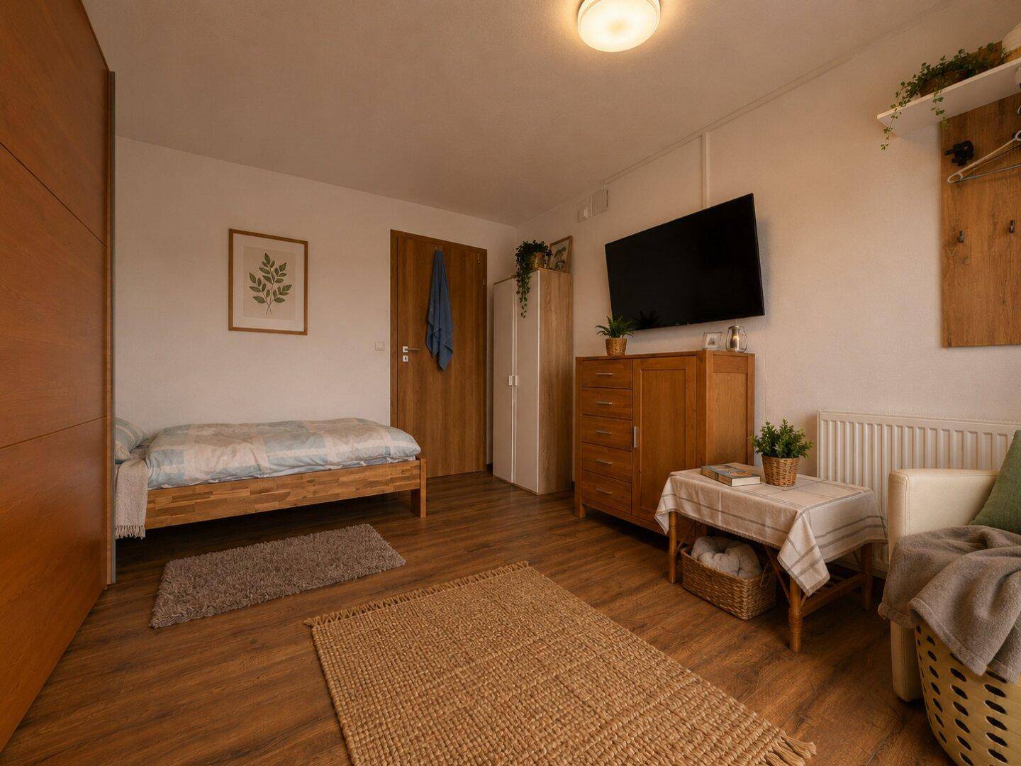 Schlafzimmer mit Holzbett, Kommode und Fernseher, hell und funktional eingerichtet.
