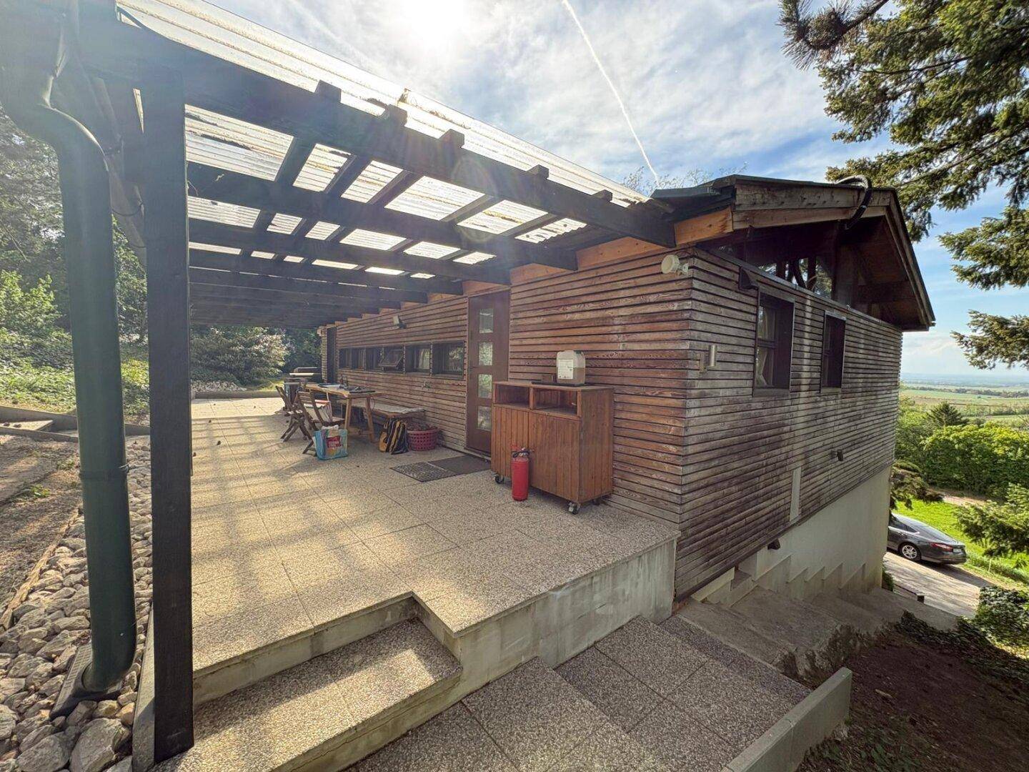 Überdachte Terrasse mit Sitzgelegenheiten und Blick auf die umliegende Landschaft, angrenzend an das Holzhaus.
