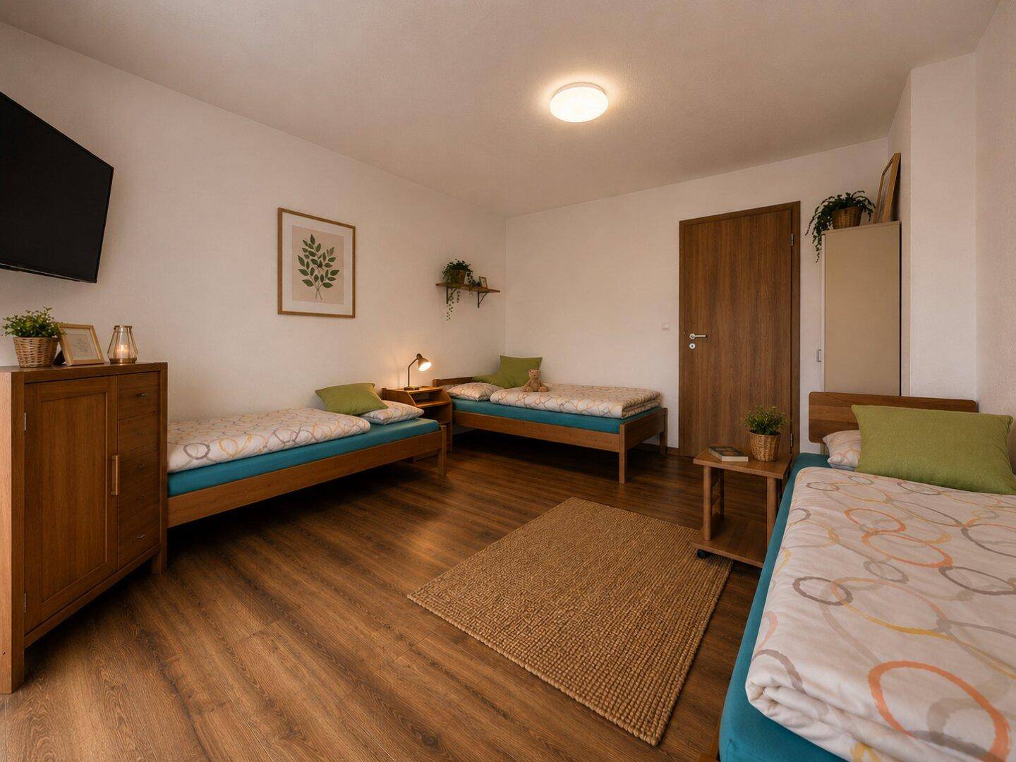 Schlafzimmer mit drei Einzelbetten, Holzboden und einfacher, funktionaler Einrichtung.