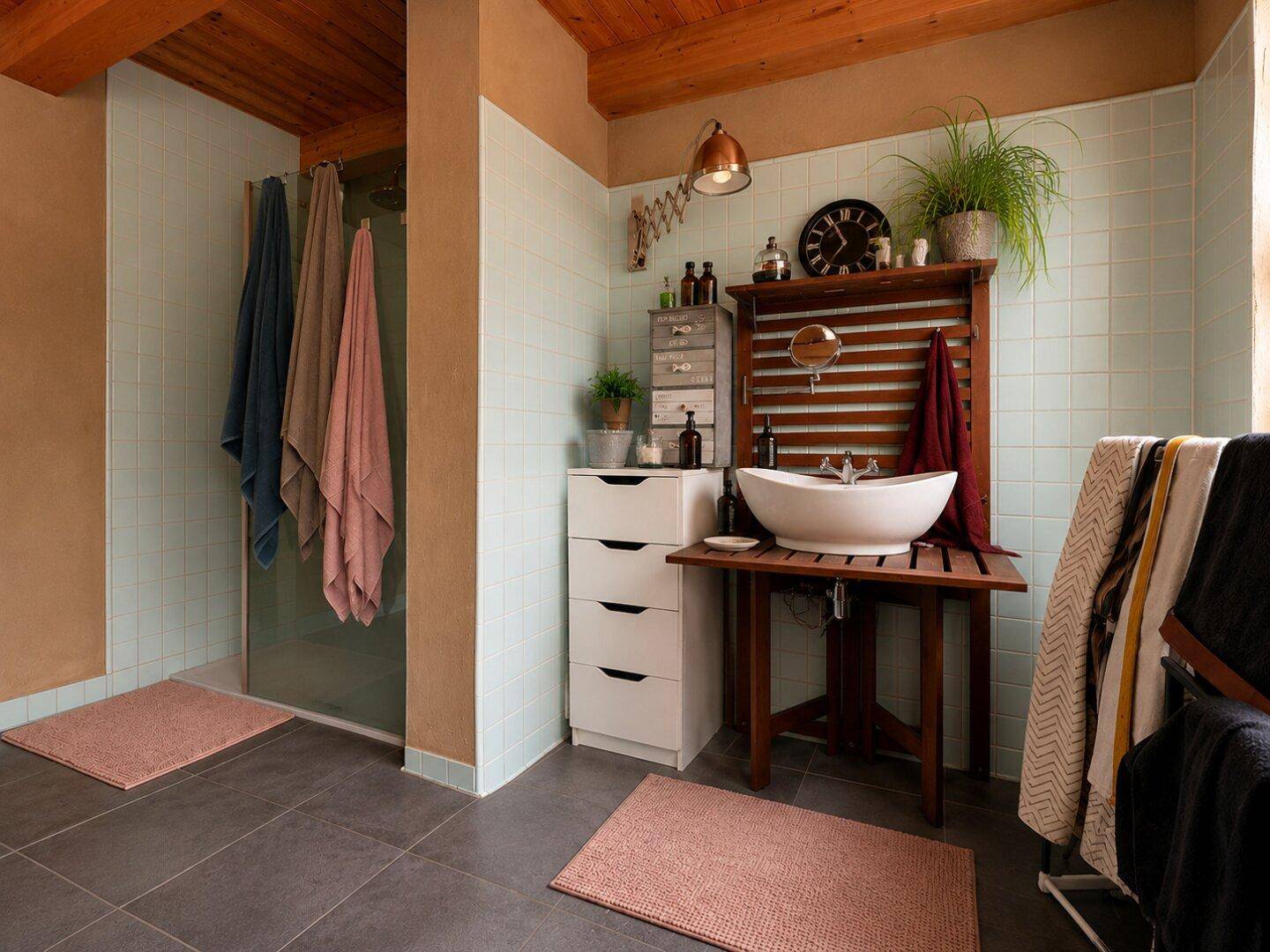 Badezimmer mit Duschkabine, Aufsatzwaschbecken, hellblauen Fliesen und einer Holzdecke.