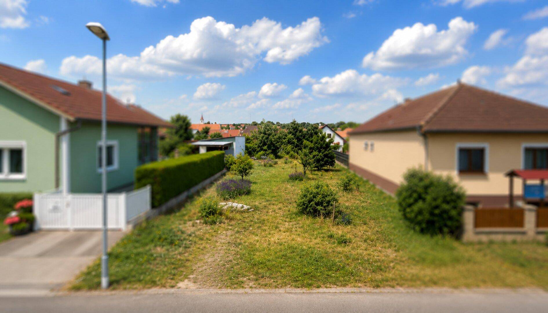 Straßenansicht einer Wohngegend mit Häusern und einer grünen Parzelle im Vordergrund.