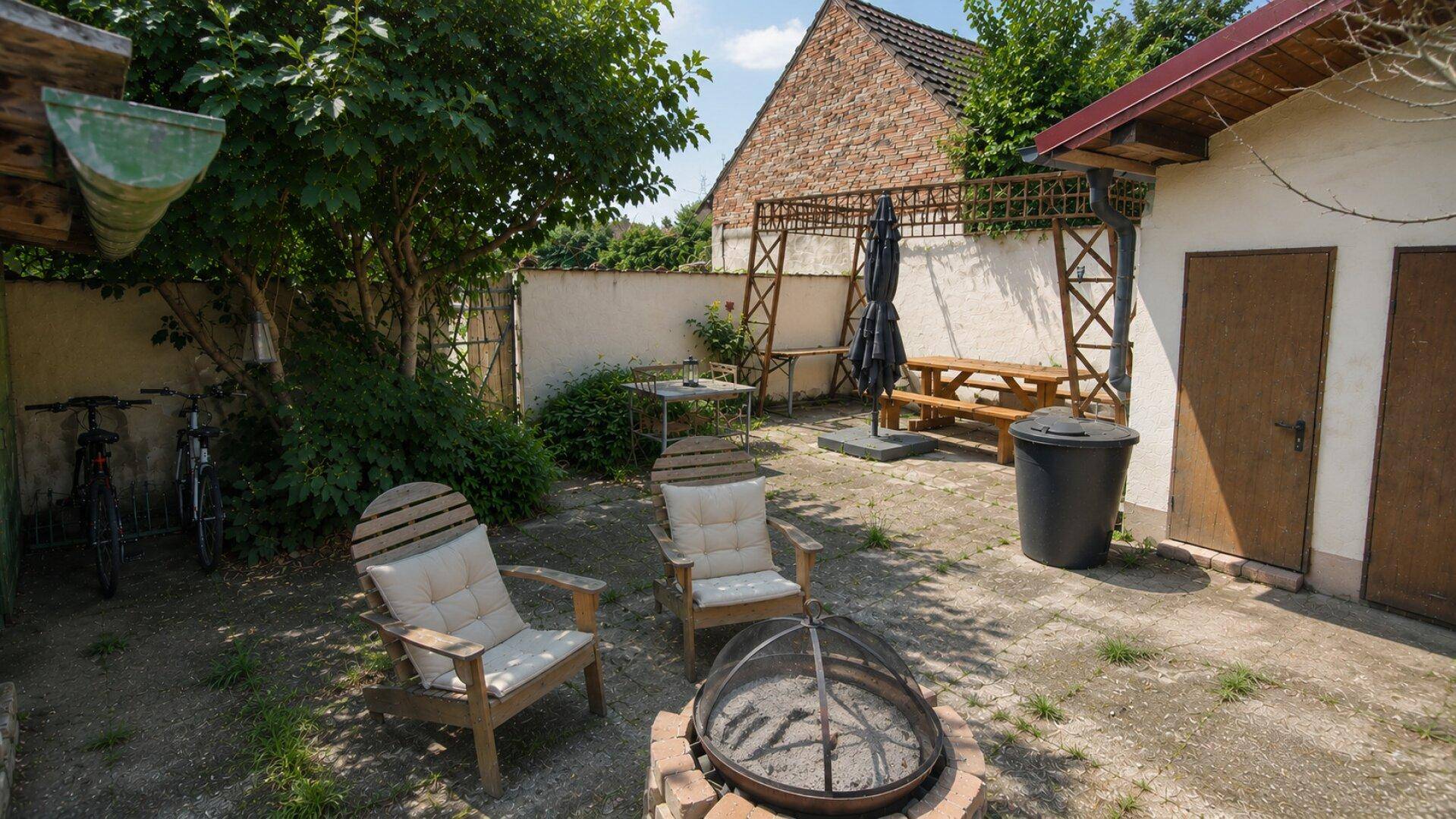 Gemütlicher Terrassenbereich mit Sitzgelegenheiten, Feuerstelle und einem kleinen Schuppen im Garten.