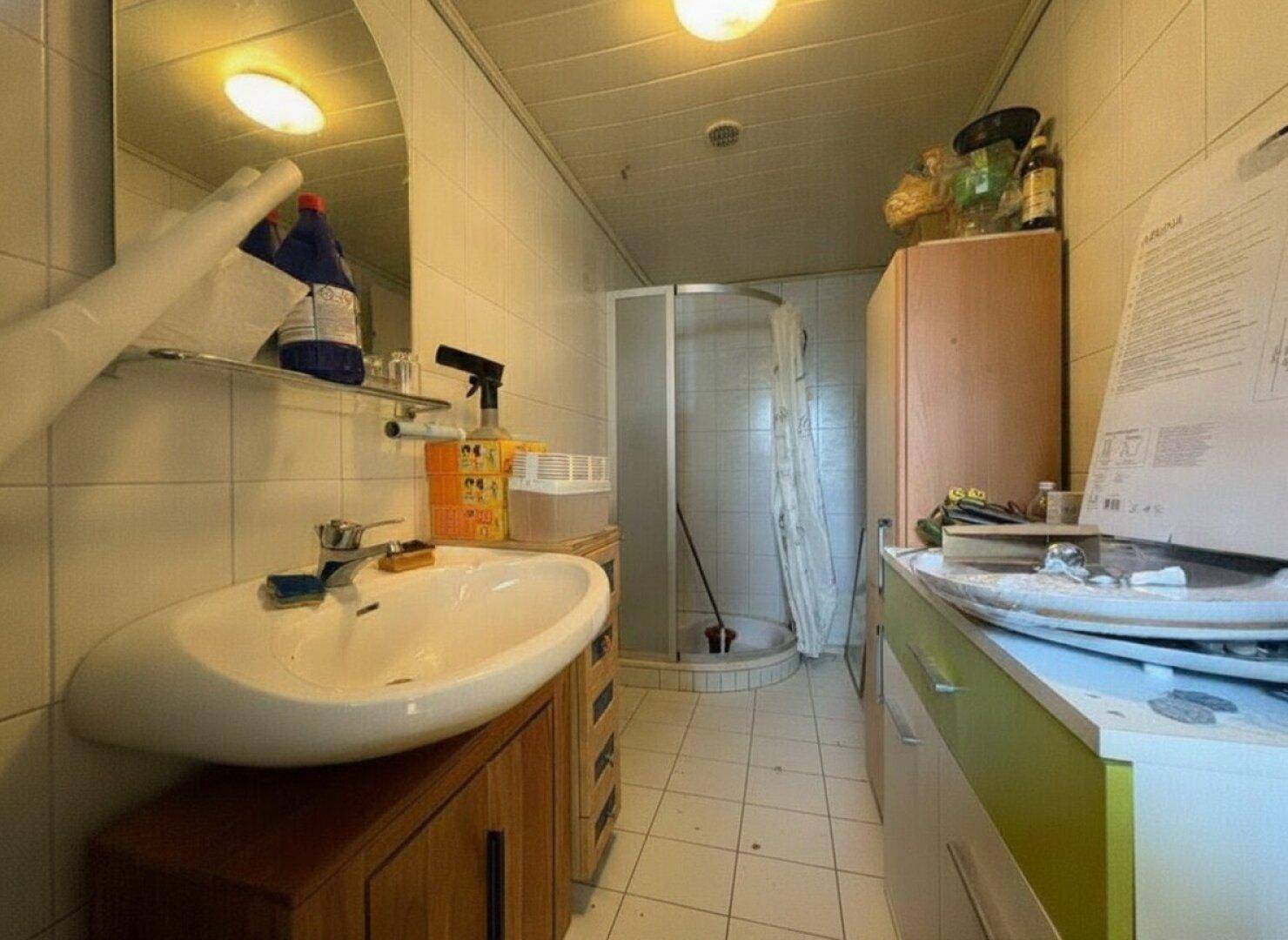 Kleines, schmales Badezimmer mit Eckdusche, Waschbecken und weißen Fliesen.