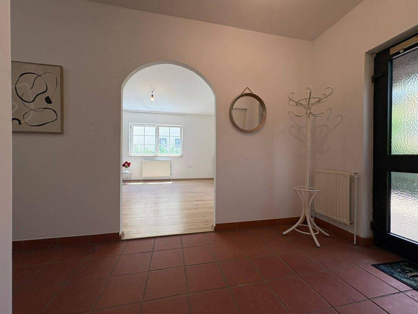 Heller Eingangsbereich mit Terrakottafliesen und einem Rundbogen, der zum Wohnbereich führt.