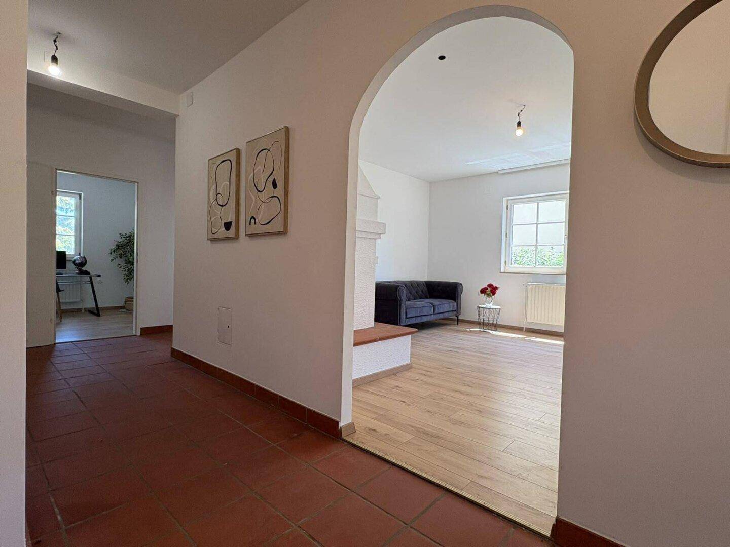 Geräumiger Flur mit Terrakottafliesen und Blick durch einen Rundbogen in das helle Wohnzimmer.