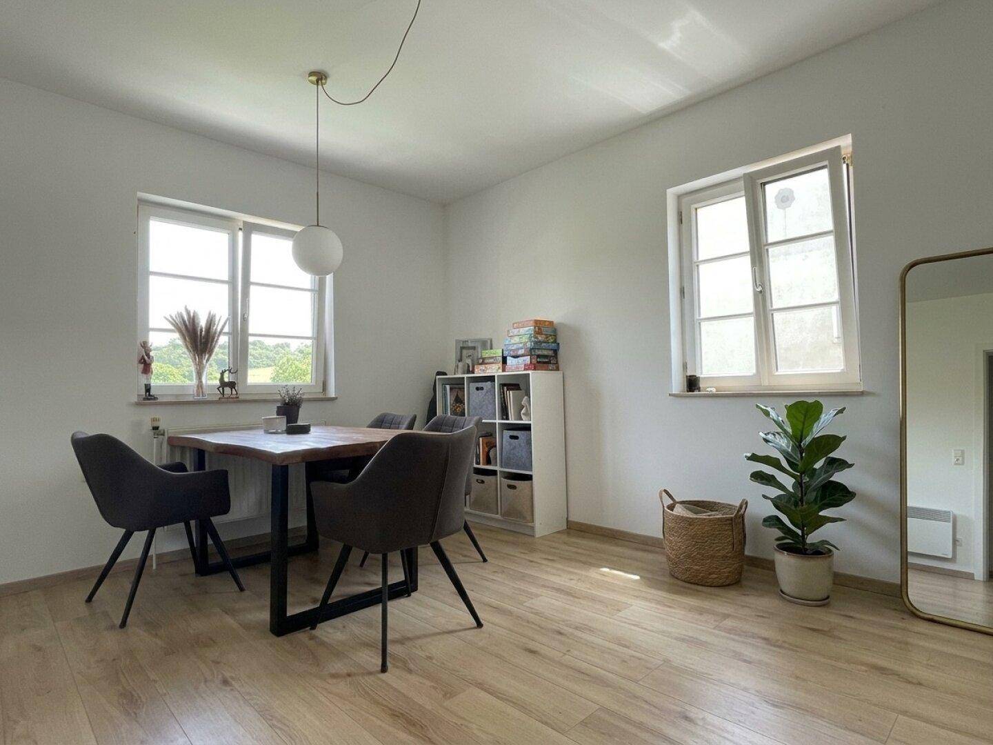 Heller Essbereich mit modernem Holztisch, Stühlen und zwei großen Fenstern.