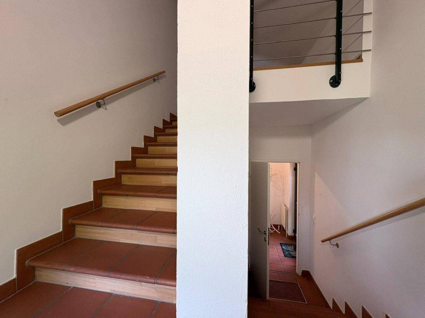 Treppenhaus mit Terrakottastufen und Holzgeländer, das die verschiedenen Ebenen verbindet.