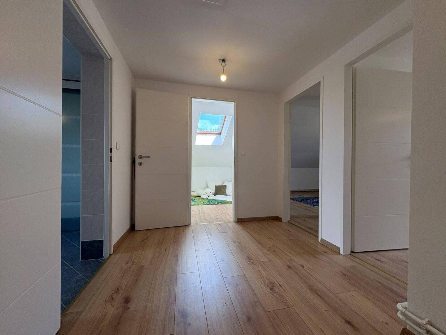 Heller Flur im Dachgeschoss mit Holzboden und Blick auf ein Dachfenster.