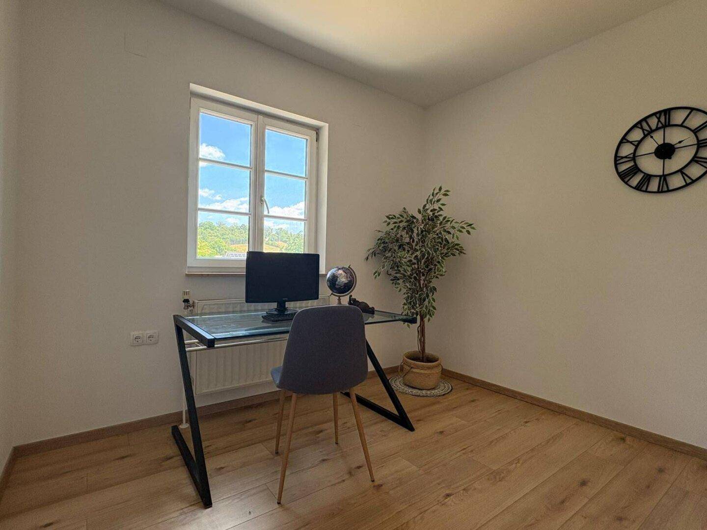 Helles Arbeitszimmer mit Schreibtisch, Stuhl und großem Fenster, ideal für Home-Office.