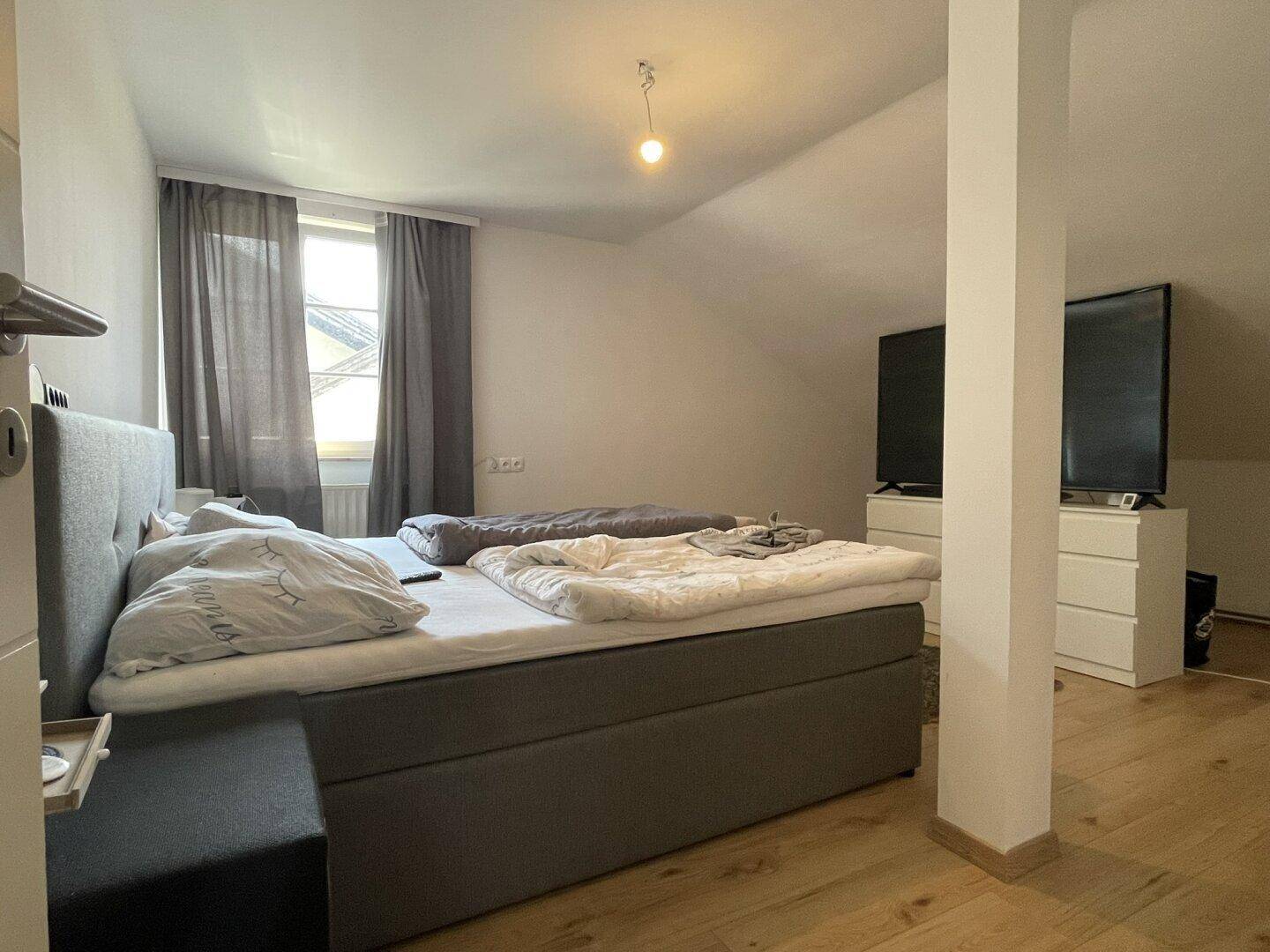 Geräumiges Schlafzimmer im Dachgeschoss mit großem Bett, Fernsehern und Fenster.