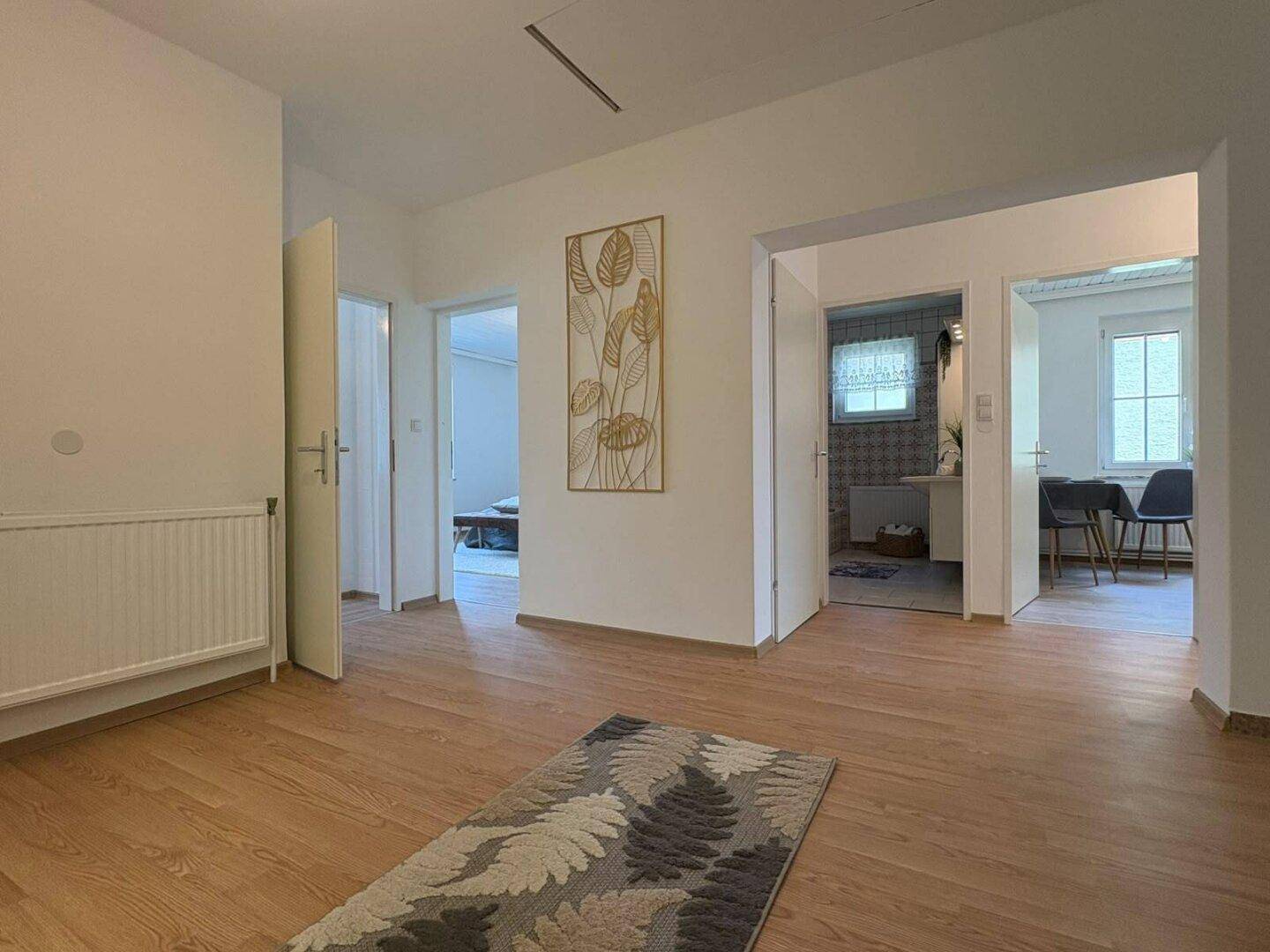 Geräumiger Flur mit Laminatboden, weiß gestrichenen Wänden und mehreren Türzugängen zu Zimmern.