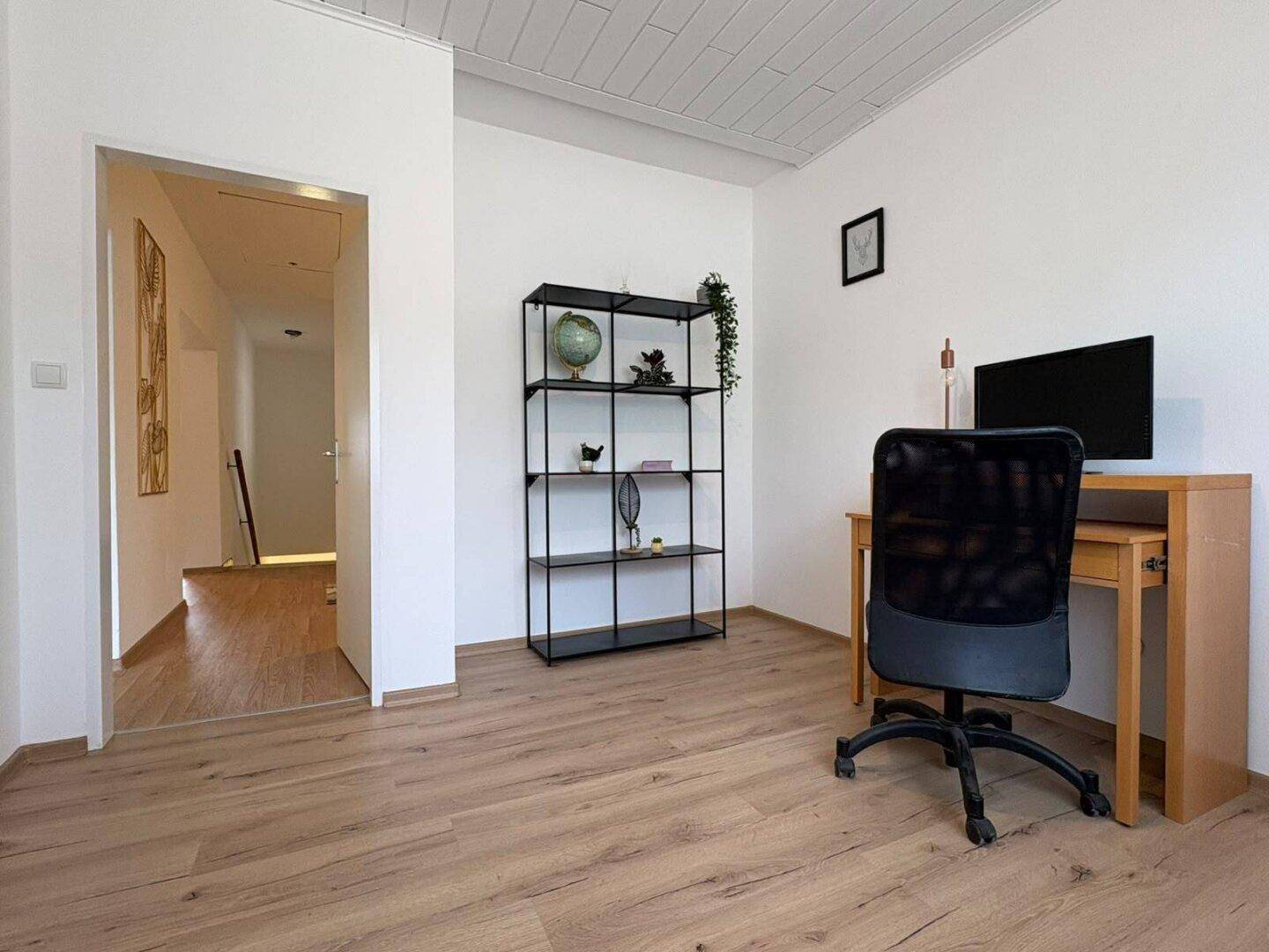 Arbeitszimmer mit Laminatboden, weiß gestrichenen Wänden und einem Regal sowie Schreibtisch.
