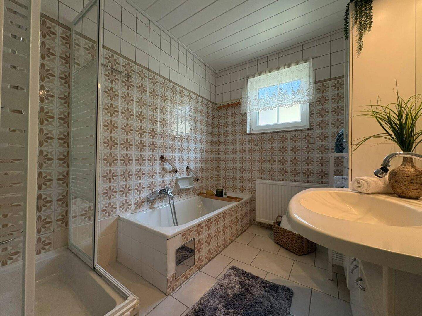 Badezimmer mit Badewanne, Duschkabine und gemusterten Fliesen im Retro-Stil der 80er Jahre.