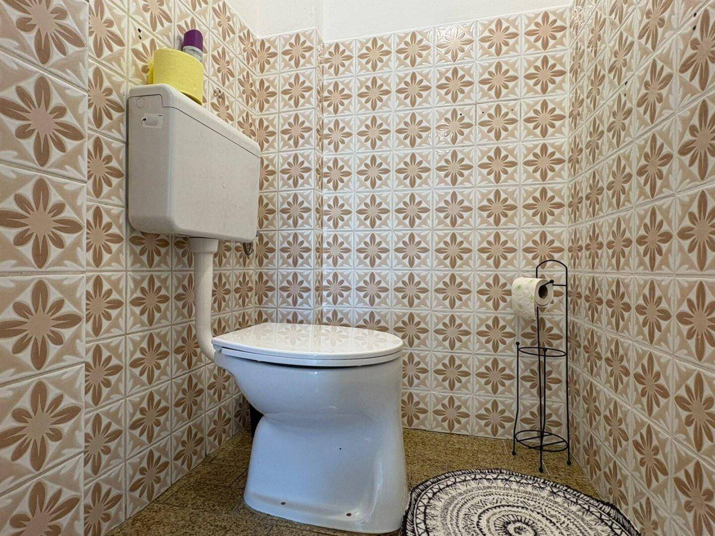 Separate Toilette mit gemusterten Fliesen im Stil der 80er Jahre und einem einfachen WC.