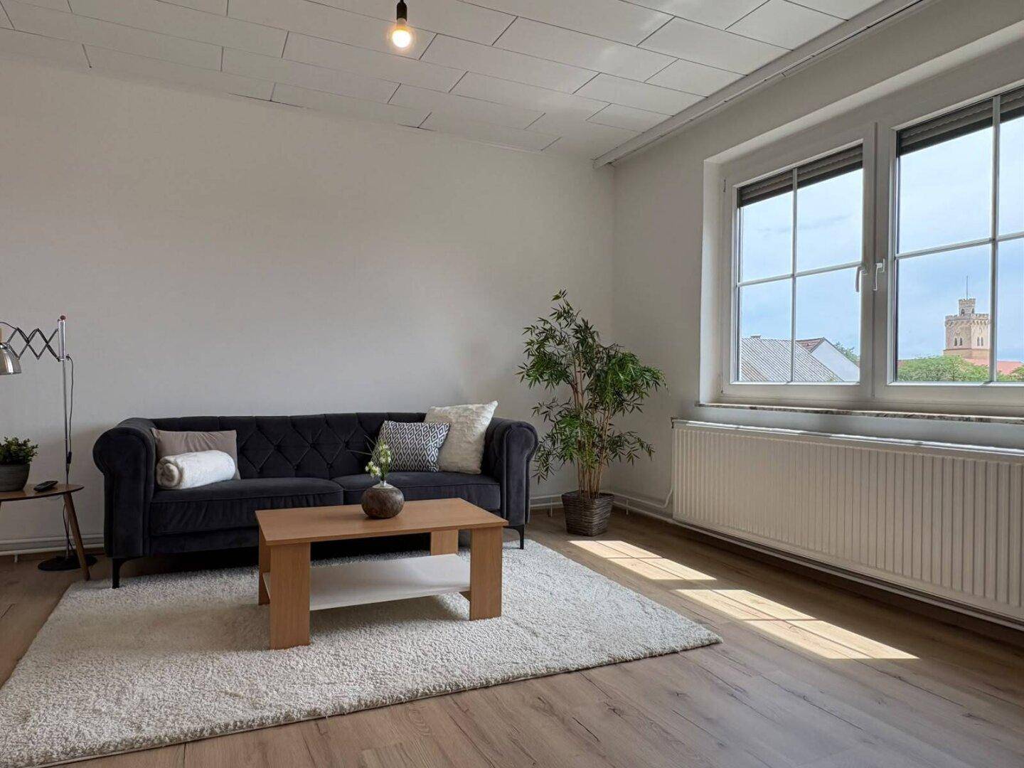 Gemütliches Wohnzimmer mit Laminatboden, bequemer Couch und großem Fenster mit Ausblick.