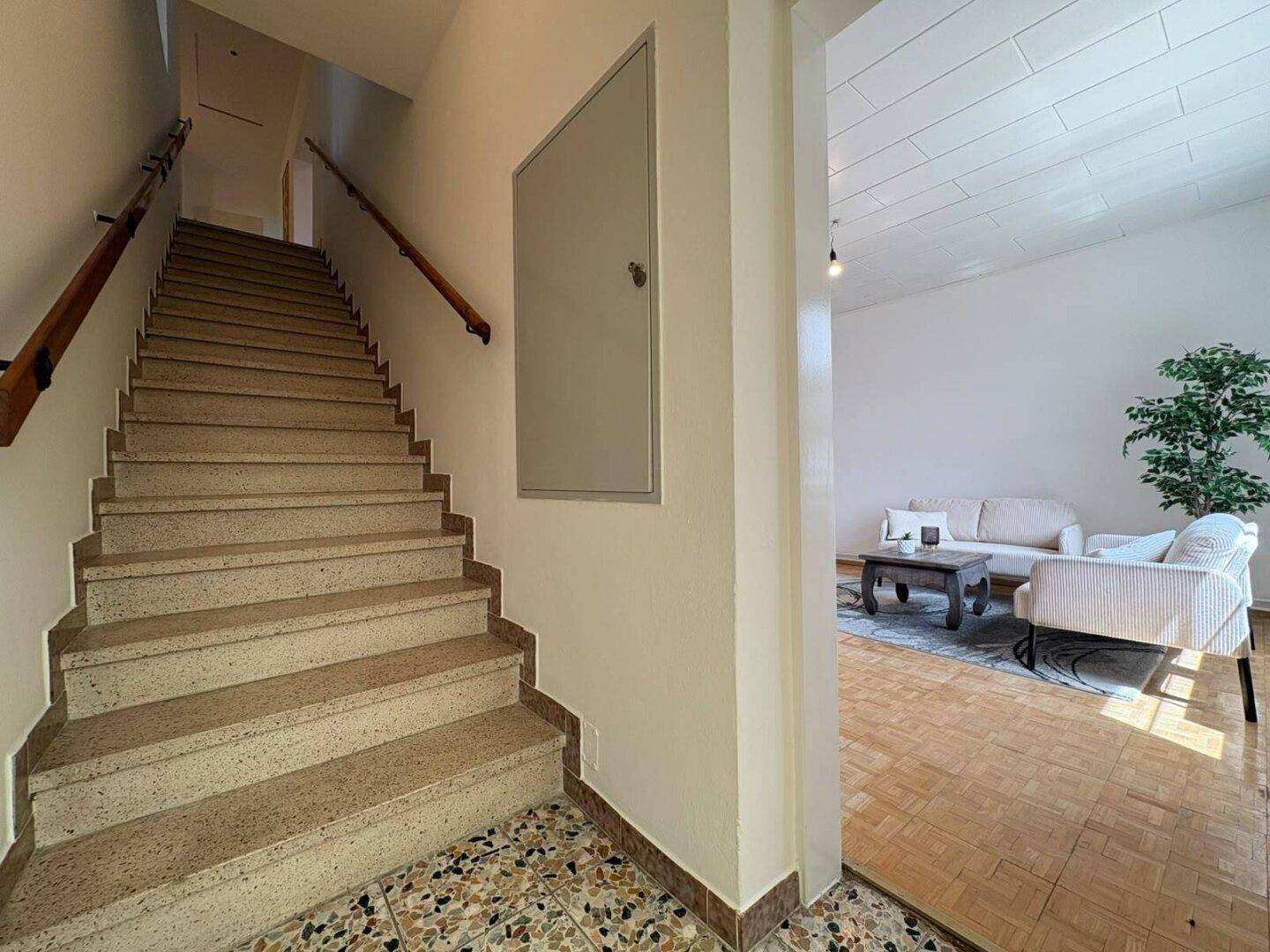Treppenhaus mit Terrazzoboden und Holzgeländer, das zu den oberen Etagen führt.