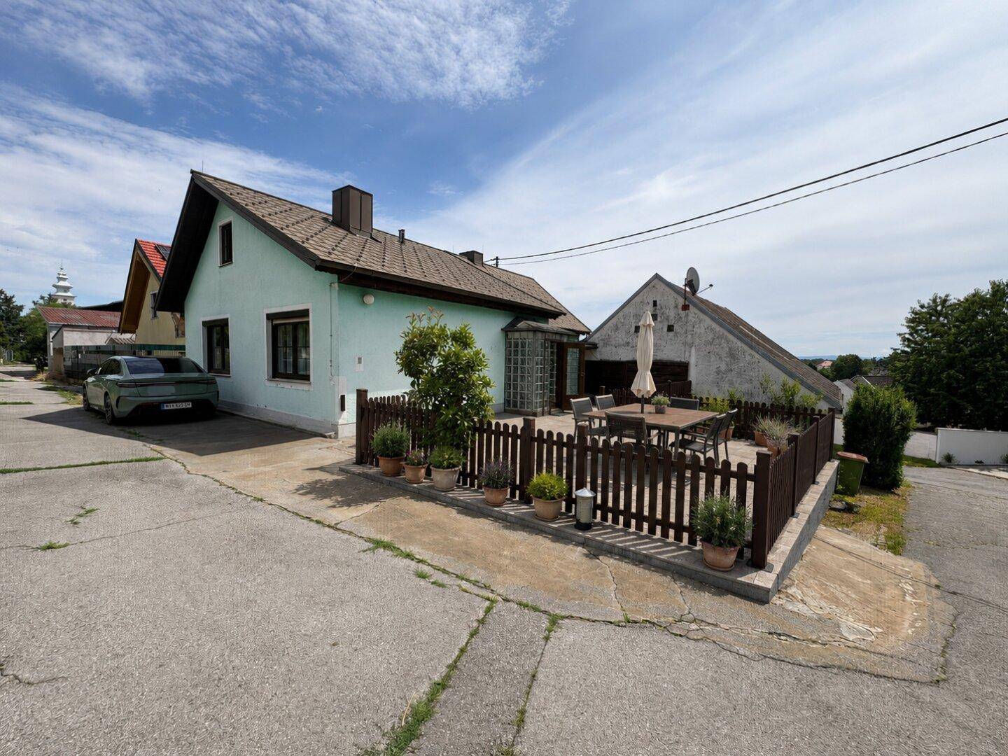Seitenansicht des Hauses mit großer gepflasterter Terrasse, Gartenmöbeln und angrenzender Auffahrt.
