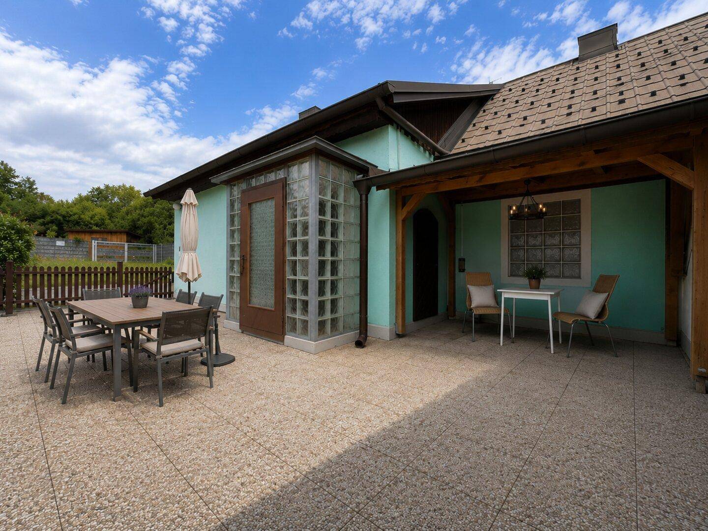 Geräumige Terrasse mit Essbereich im Freien, Sonnenschirm und überdachtem Sitzbereich am Haus.