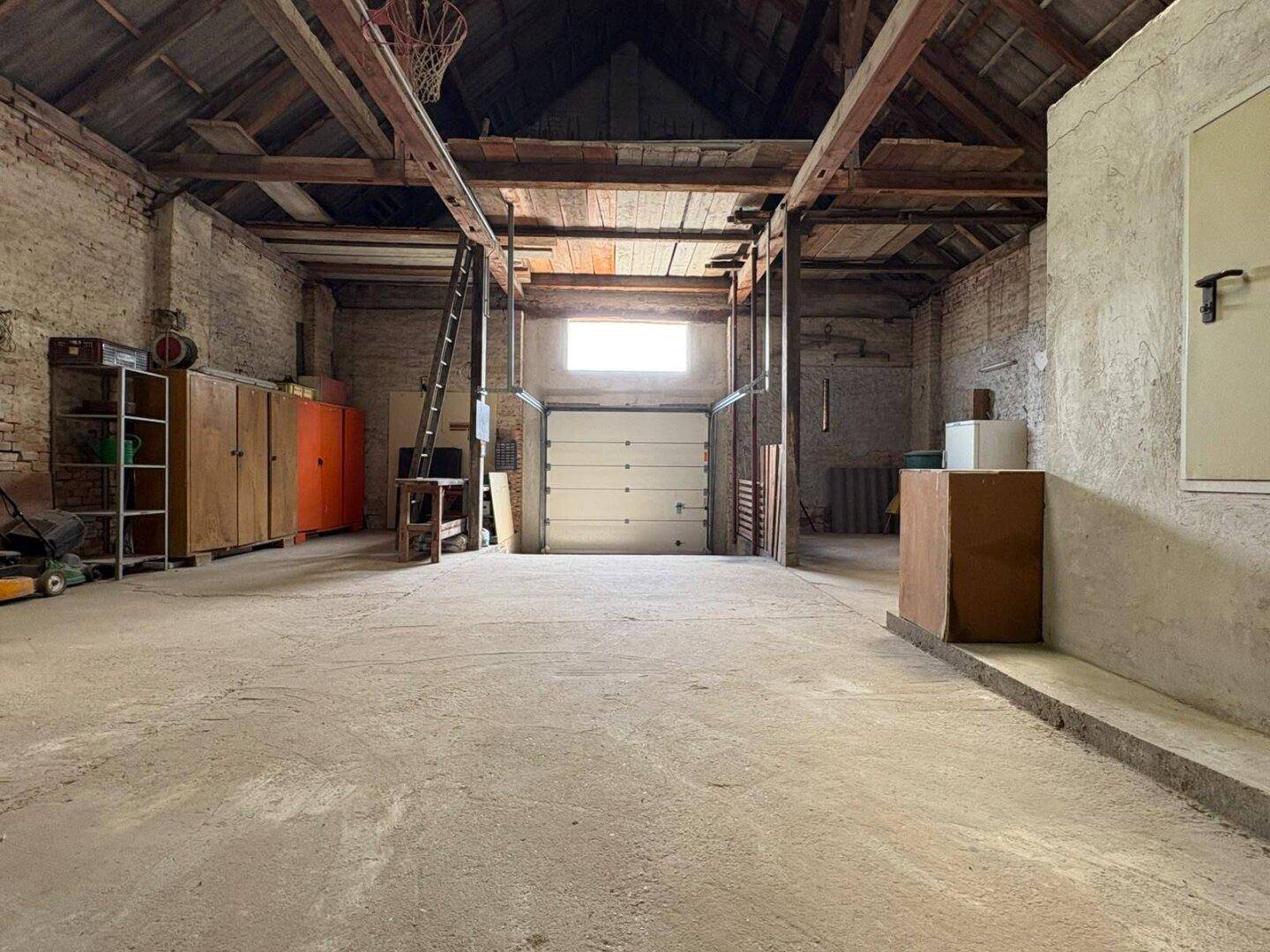 Geräumige Garage oder Scheune mit hohen Decken, sichtbaren Holzbalken und Betonboden.