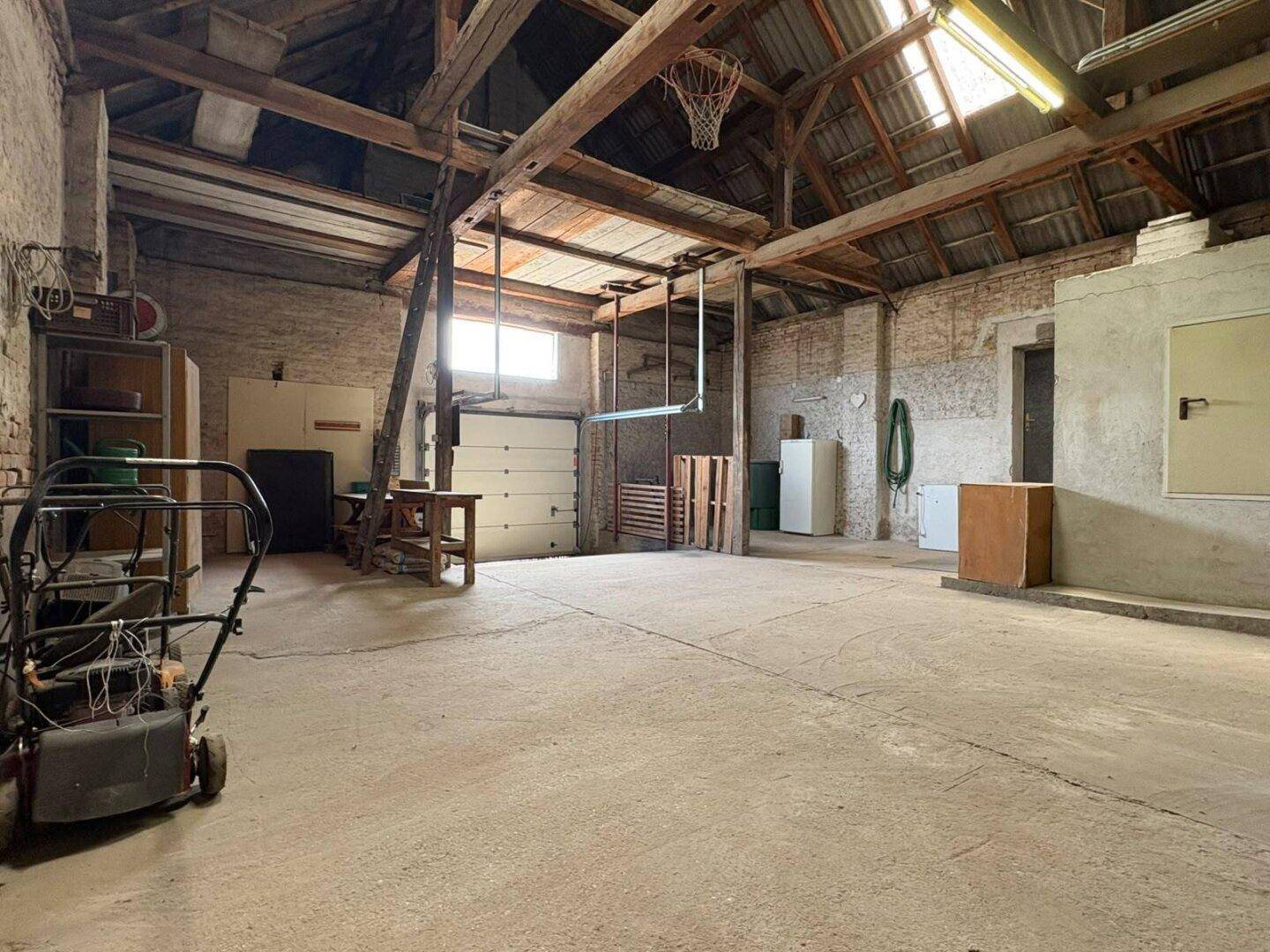 Großer Lagerraum oder Garage mit offenem Dachstuhl, Betonboden und verschiedenen Abstellmöglichkeiten.