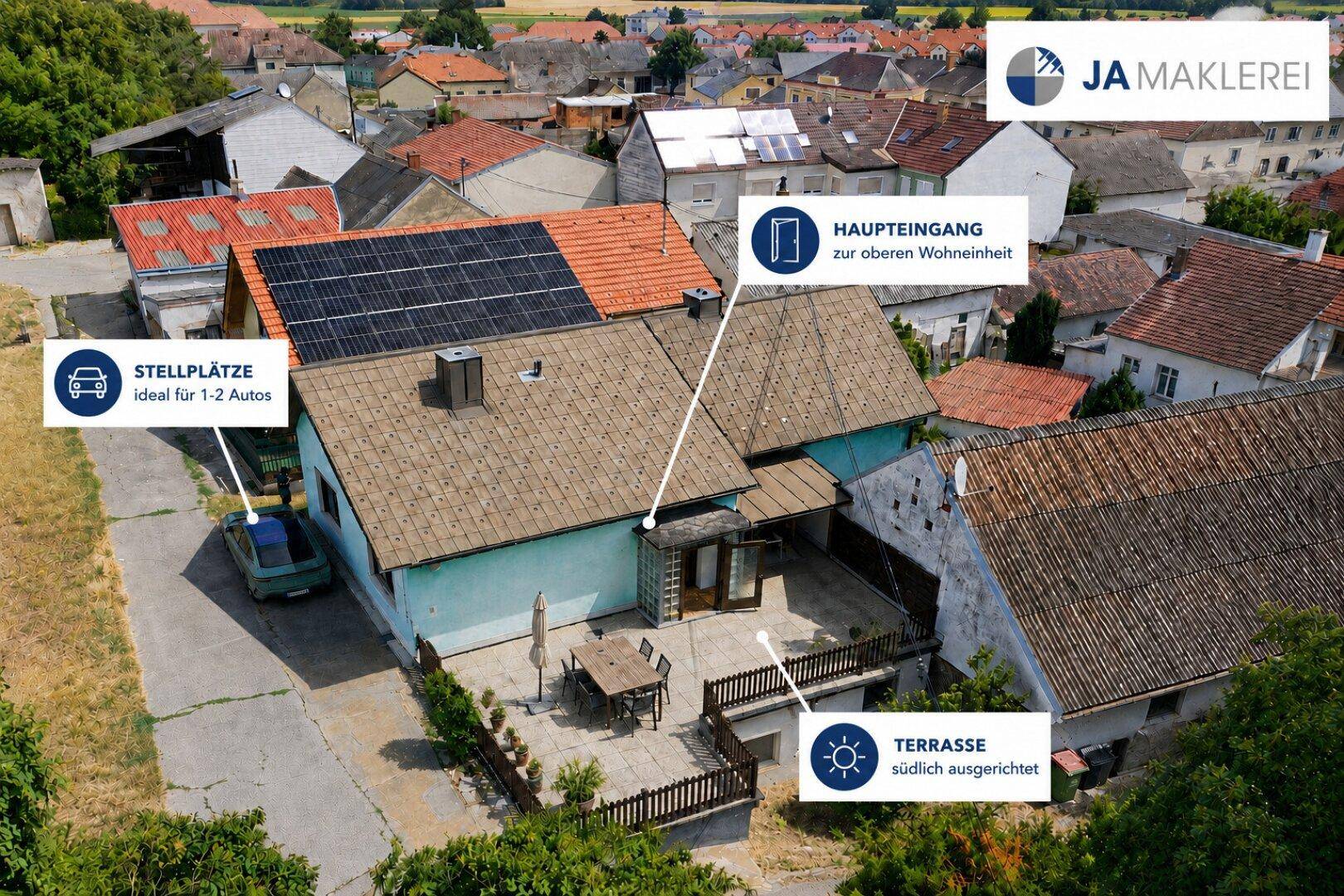 Luftaufnahme des Anwesens mit Haus, südlich ausgerichteter Terrasse, Stellplätzen und Solaranlage auf dem Dach.