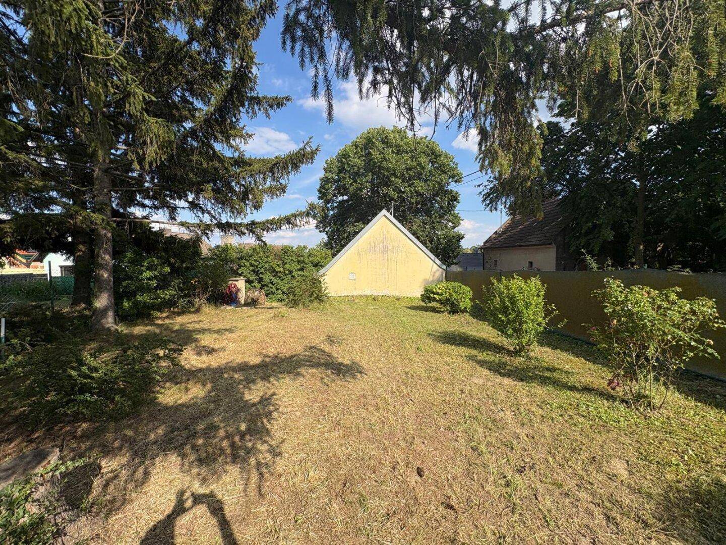 Weitläufiger Garten mit altem Baumbestand, Rasenfläche und Blick auf ein kleines Nebengebäude.
