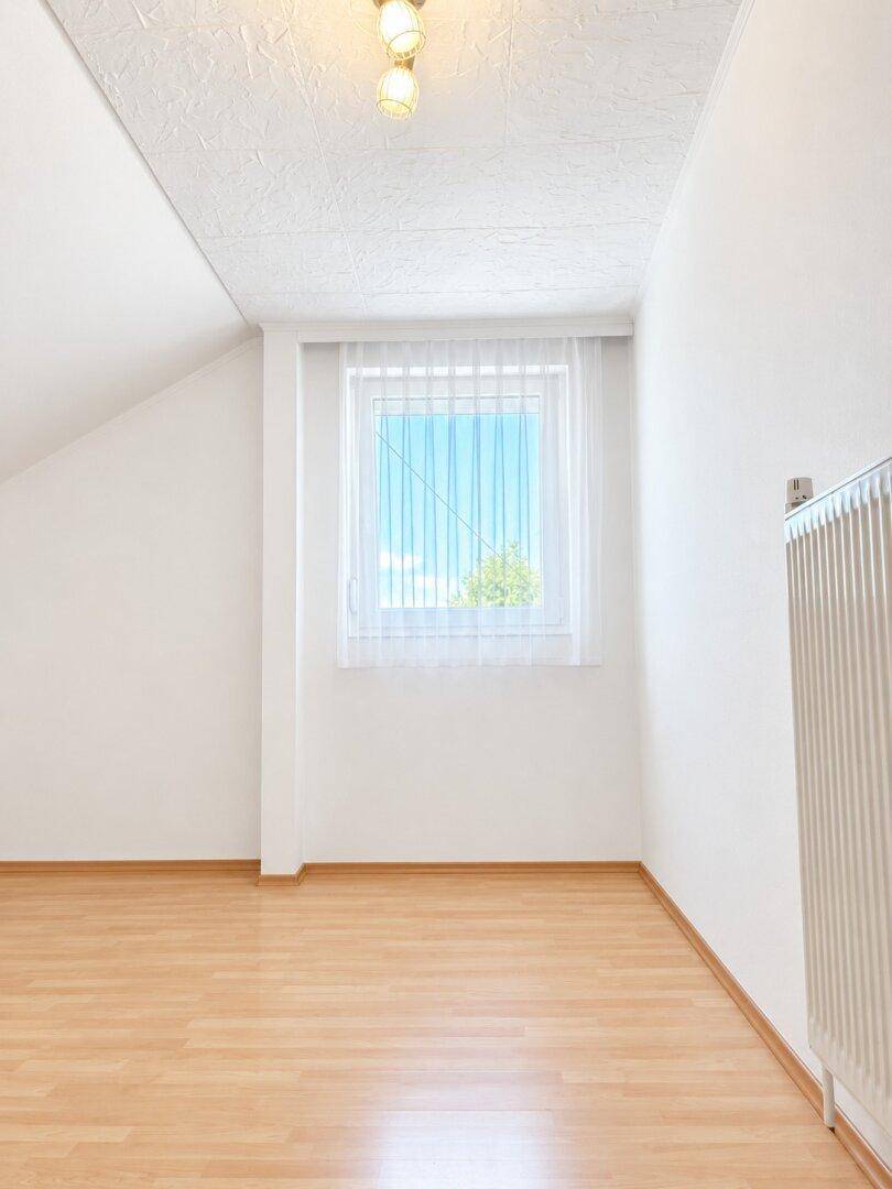 Helles Zimmer im Dachgeschoss mit schräger Decke und Laminatboden.