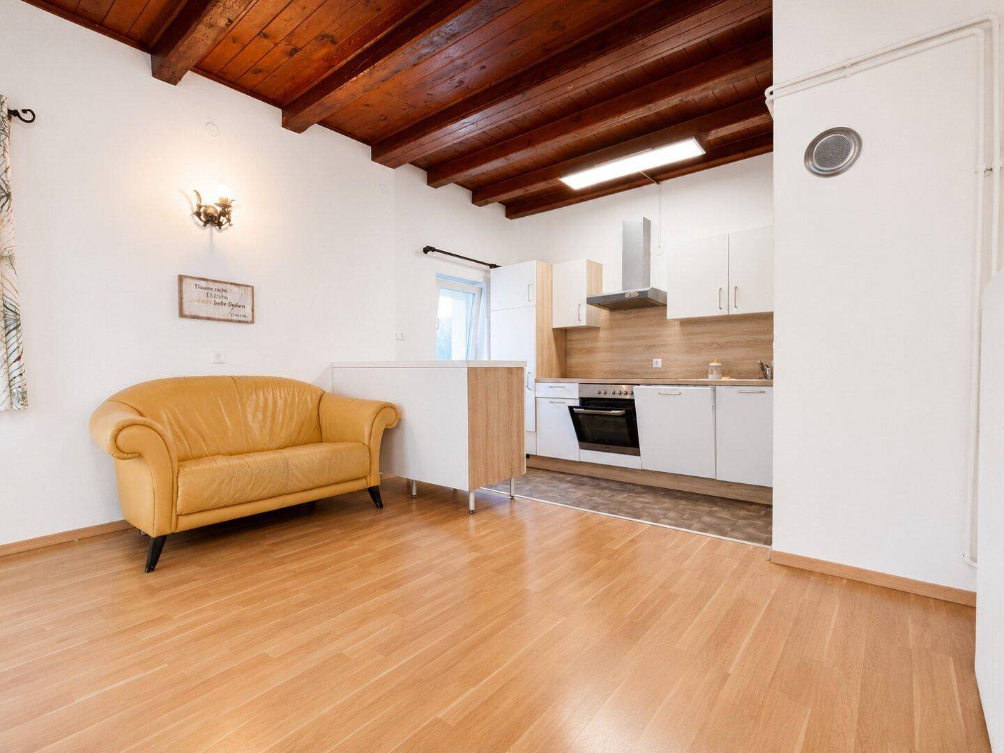 Gemütlicher Wohnbereich mit gelbem Sofa, Holzbalkendecke und offener Küchenzeile.