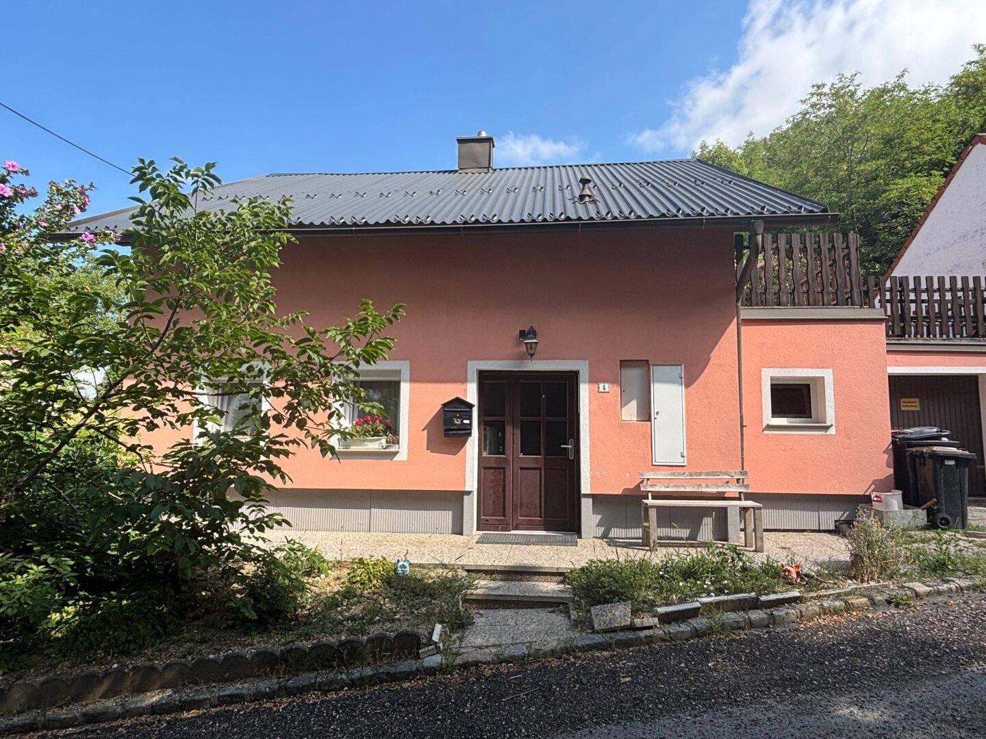 Vorderansicht des rosa gestrichenen Hauses mit Eingangstür und kleinen Fenstern.
