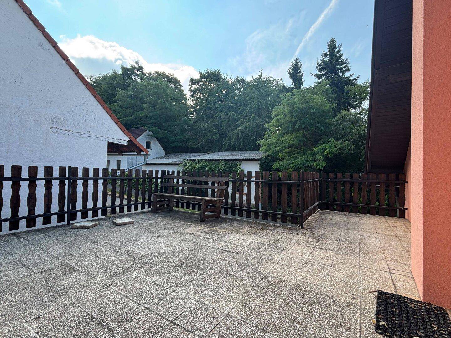 Weitläufige Terrasse mit Holzzaun und Sitzbank, umgeben von viel Grün.