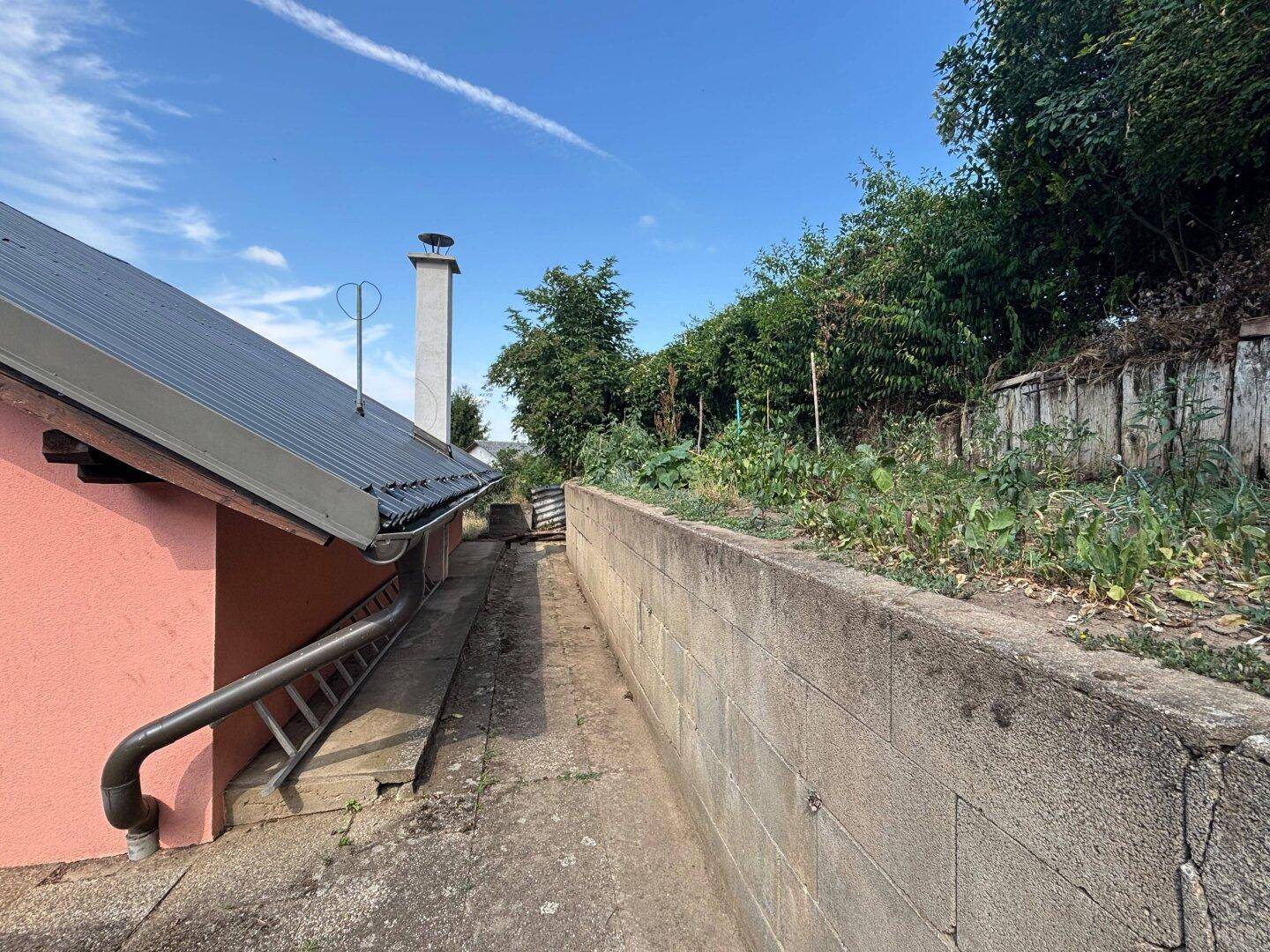 Schmaler Weg entlang der Hauswand mit Treppe und Blick auf die Umgebung.