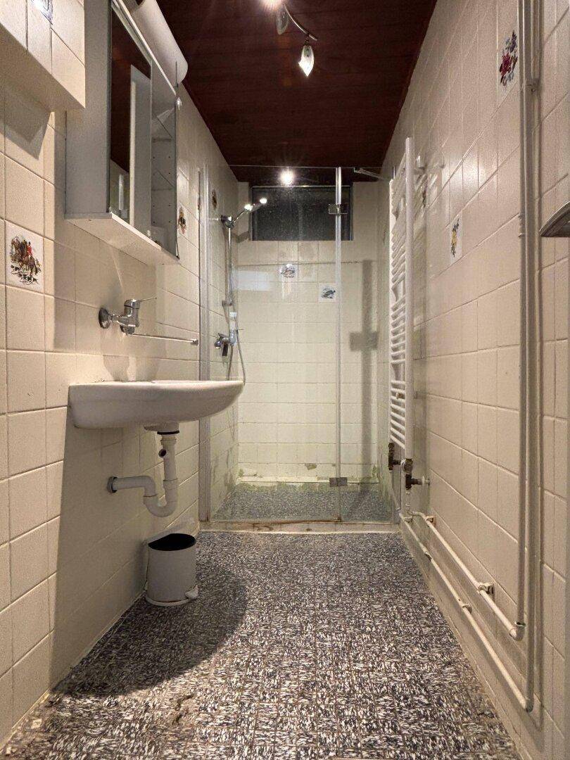 Schlichtes Badezimmer mit Dusche, Waschbecken und gefliesten Wänden.