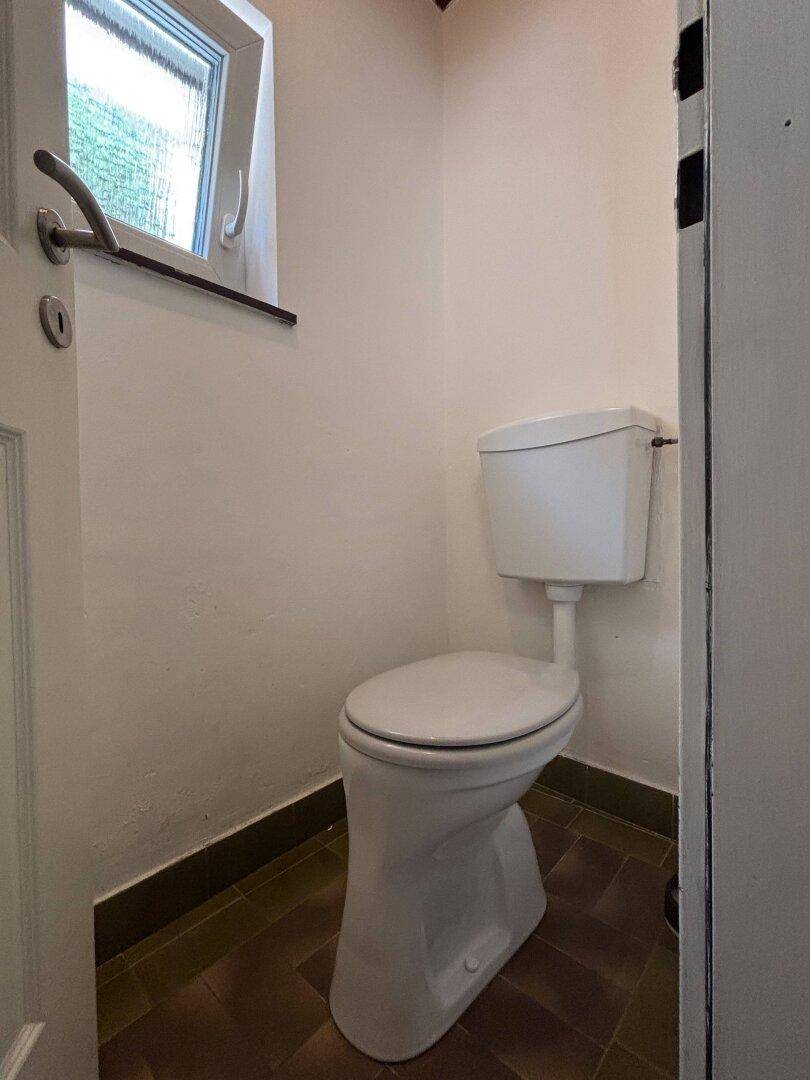 Kleines WC mit Fenster, Toilette und dunklen Bodenfliesen.