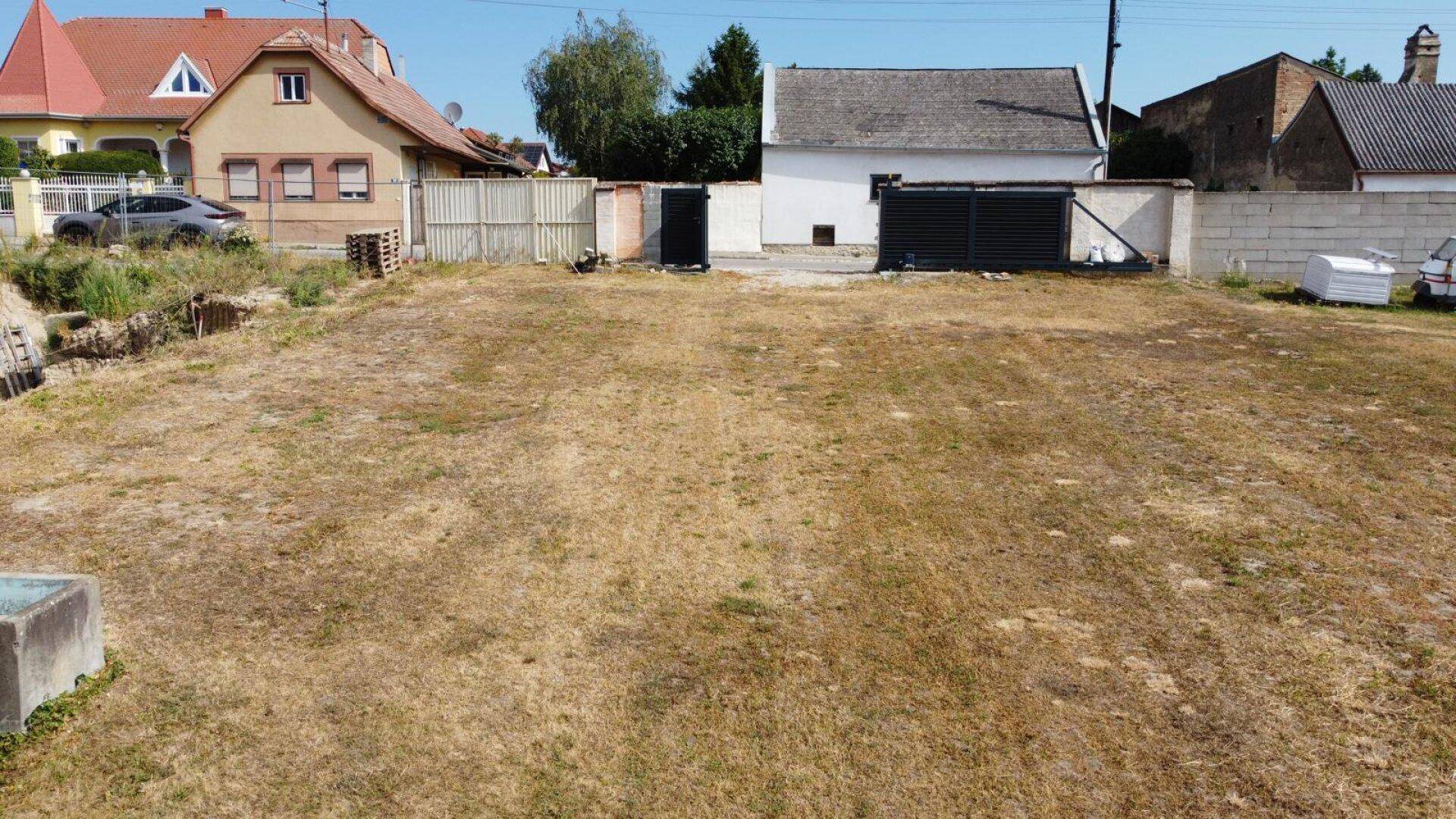 Weitläufiges Grundstück mit trockenem Rasen und angrenzenden Wohnhäusern, ideal für Neubauprojekte.