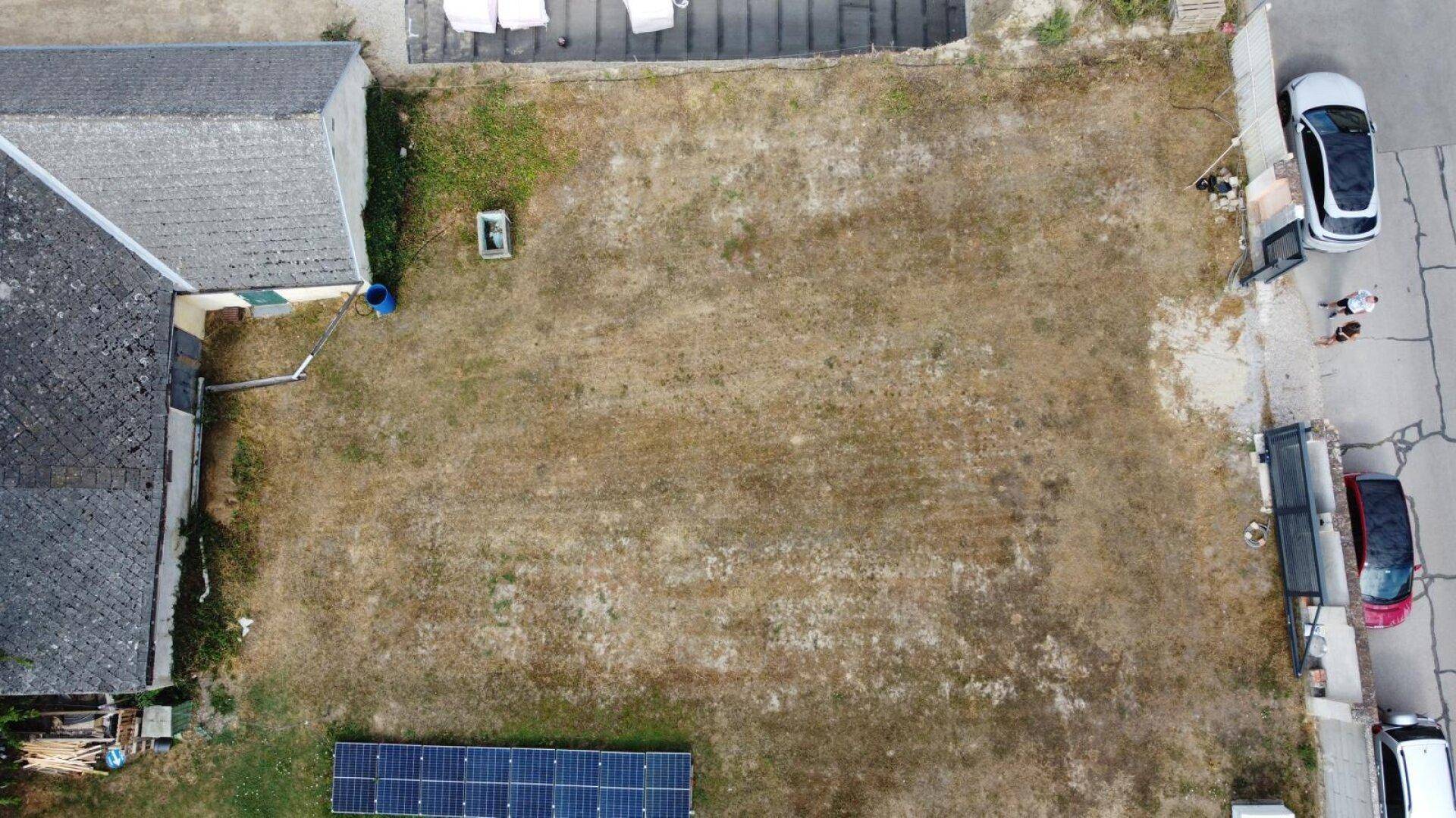 Luftaufnahme eines Grundstücks mit trockenem Rasen, Nebengebäude und einer Photovoltaikanlage auf dem Dach.