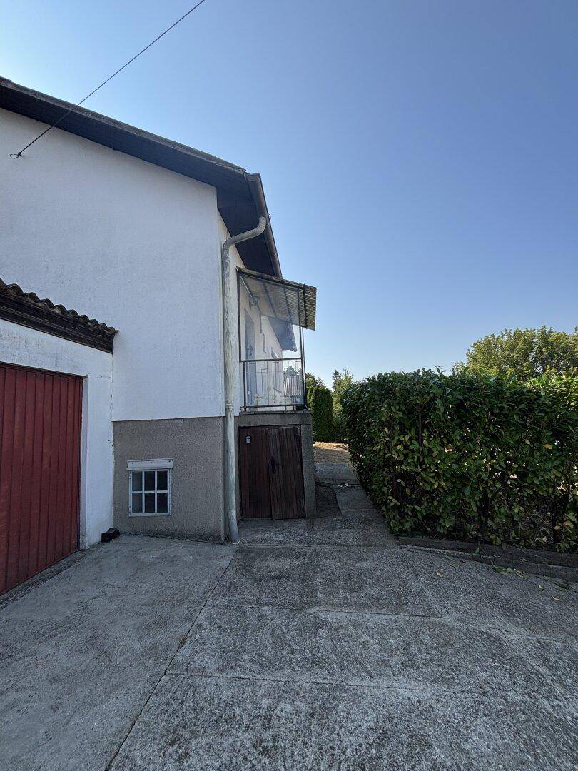 Seitenansicht des Hauses mit Zufahrt, kleinem Balkon und üppiger Hecke.