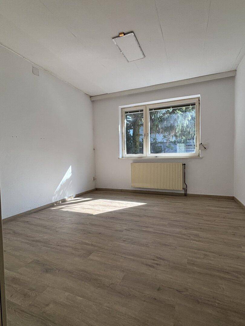 Helles Zimmer mit neuem Laminatboden, weiß gestrichenen Wänden und großem Fenster.