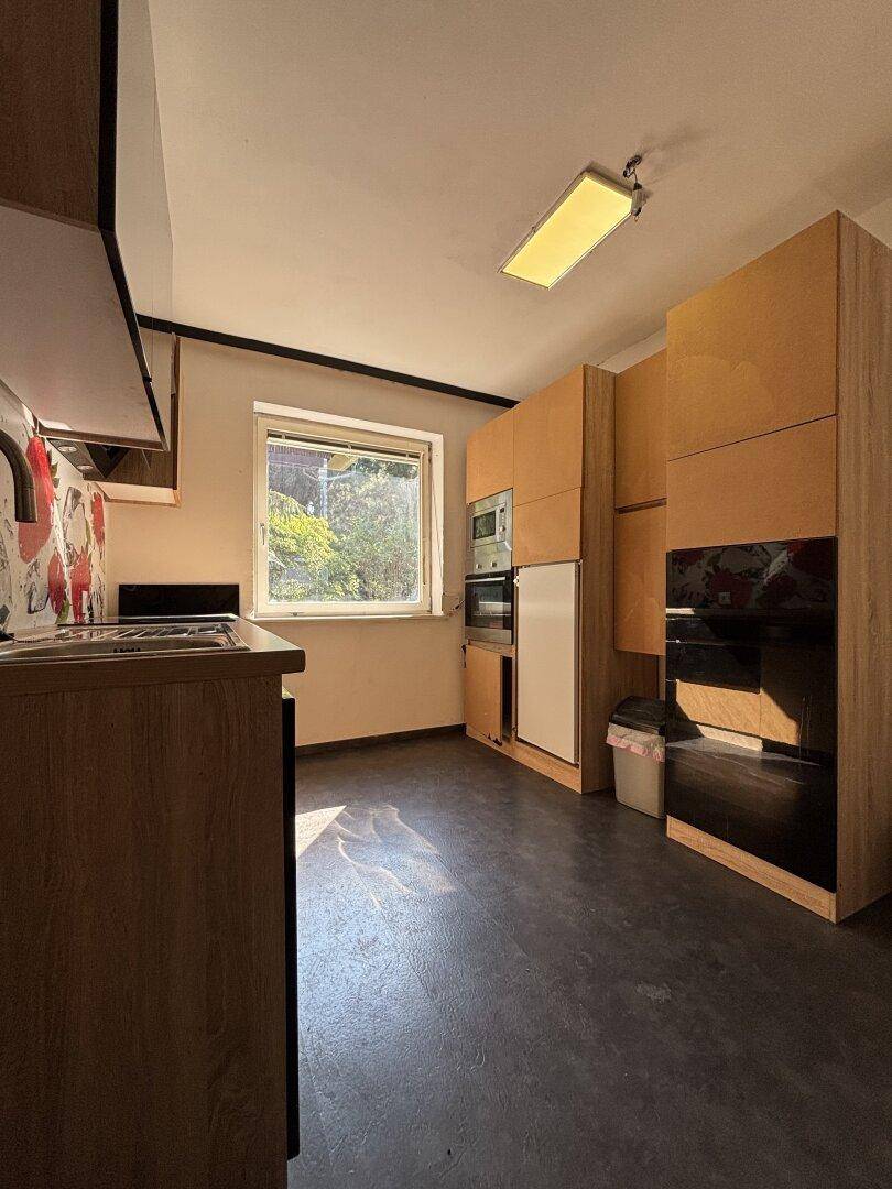 Funktionale Küche mit Holzschränken, integrierten Geräten und Fenster mit Blick ins Grüne.