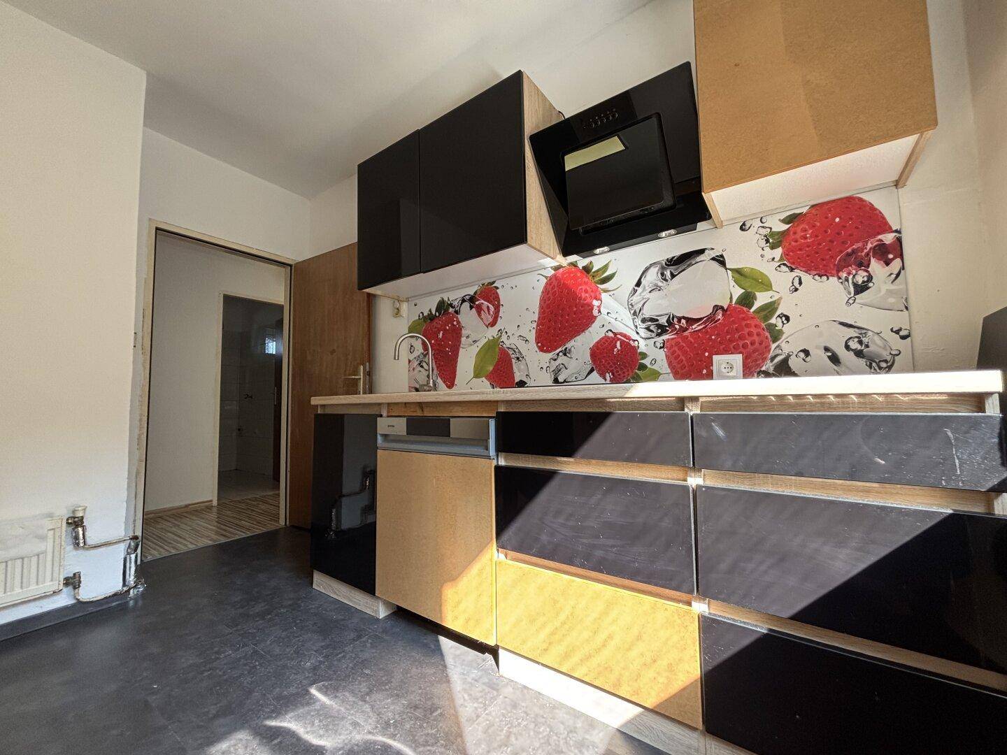 Moderne Küche mit schwarzen Hochglanzfronten, Holzakzenten und auffälliger Erdbeer-Rückwand.