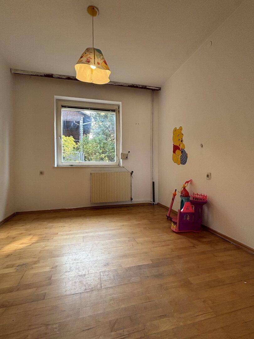 Kinderzimmer mit Holzparkett, Fenster und Wanddekoration, bereit zur individuellen Gestaltung.