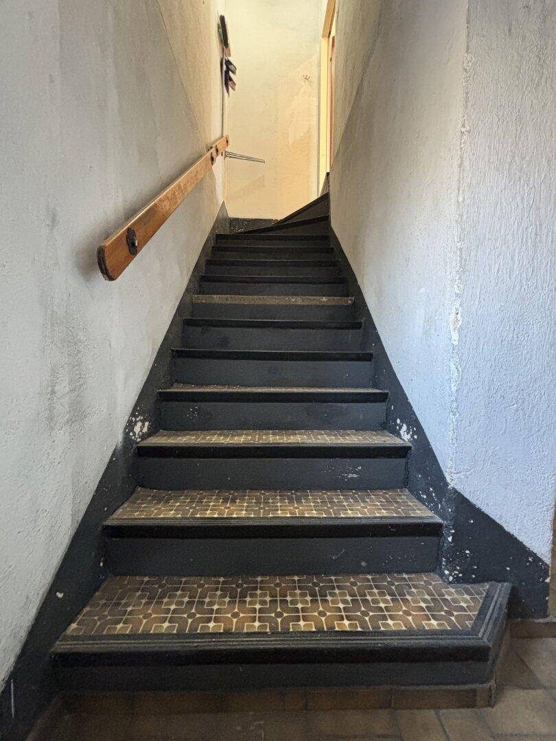 Treppenhaus mit Holzgeländer und gefliesten Stufen, das die Etagen verbindet.