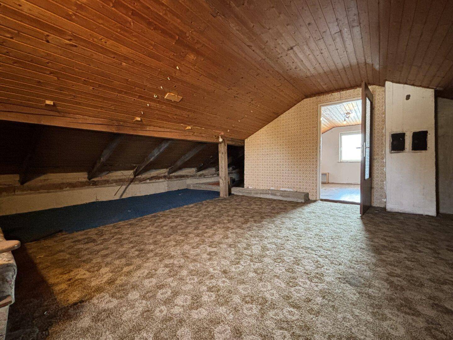 Ausbaufähiger Dachboden mit Holzverkleidung und Teppichboden, bietet viel Potenzial.