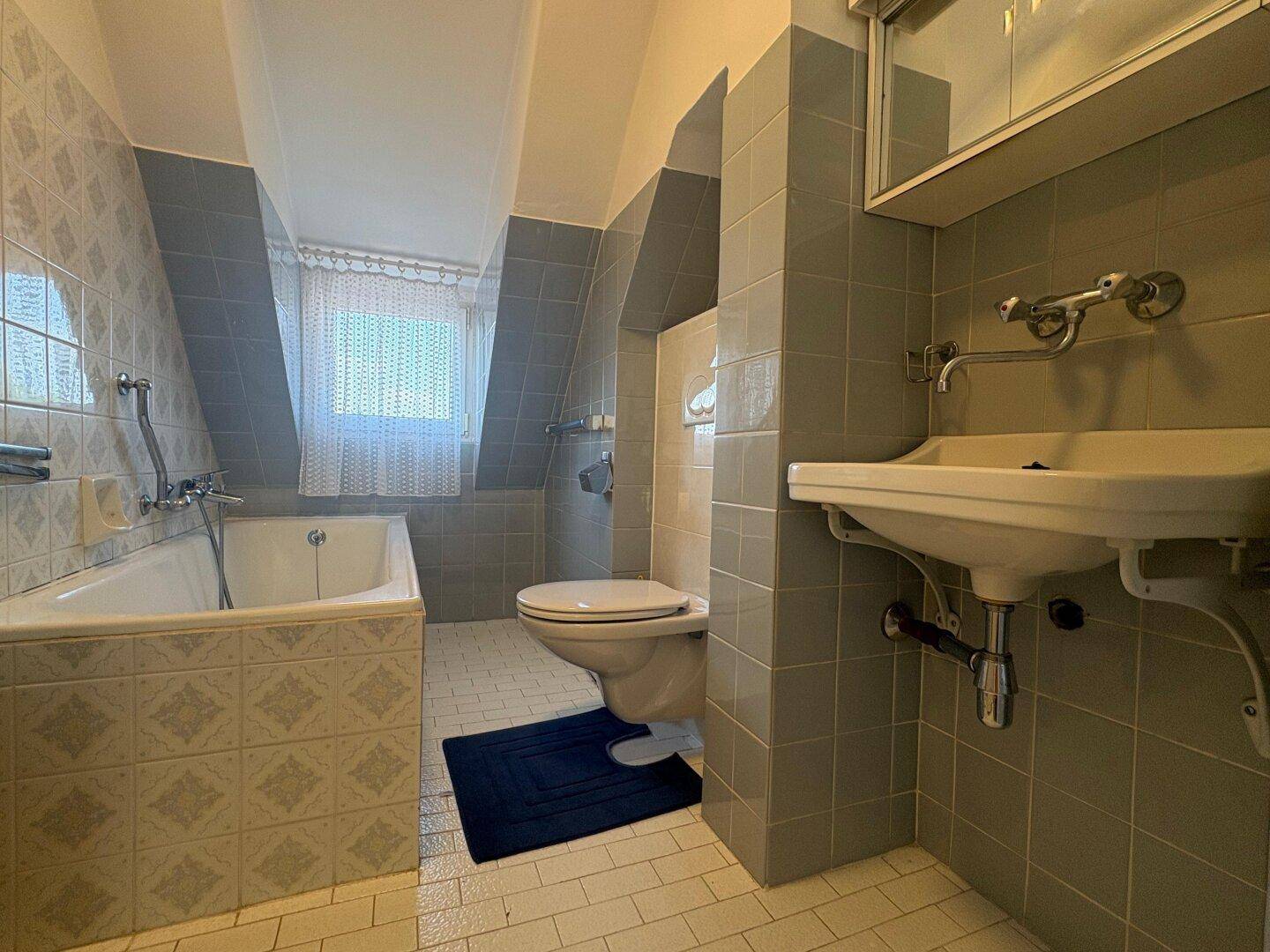 Badezimmer im Dachgeschoss mit Badewanne, Toilette und grauen Fliesen.