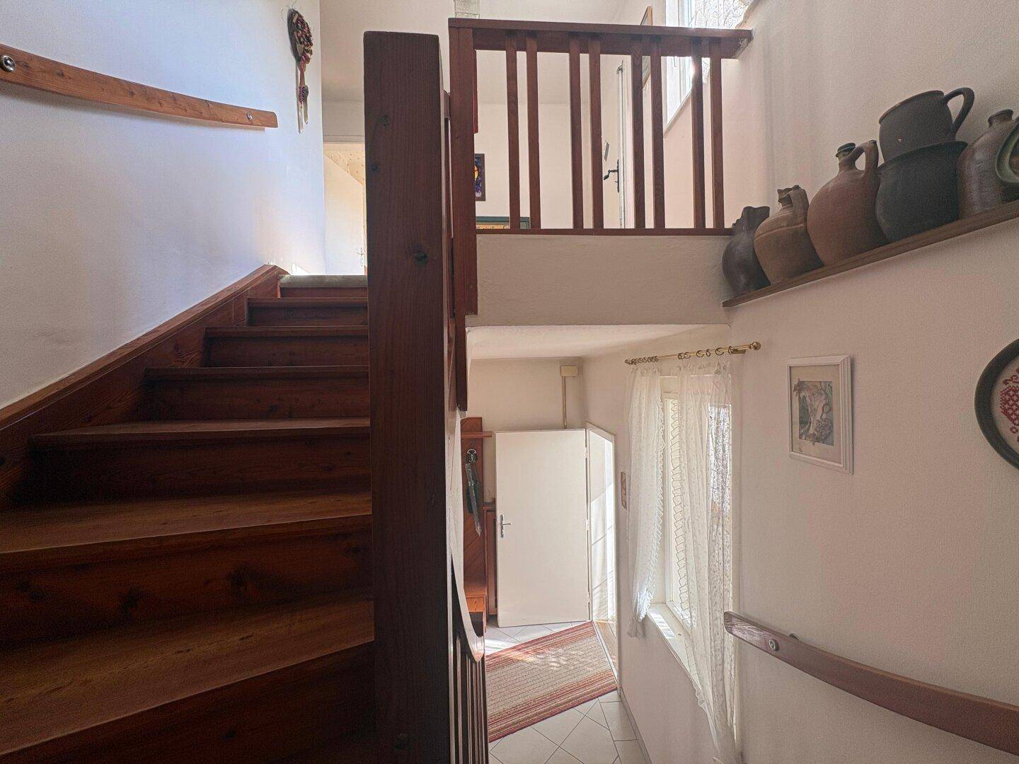 Holztreppe führt in den oberen Stock, dekoriert mit traditionellen Keramikgefäßen.