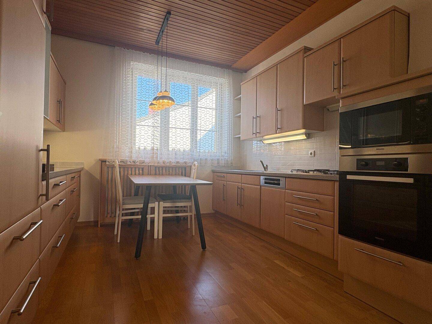 Funktionale Küche mit Holzboden, Einbauküche und Essbereich am Fenster.